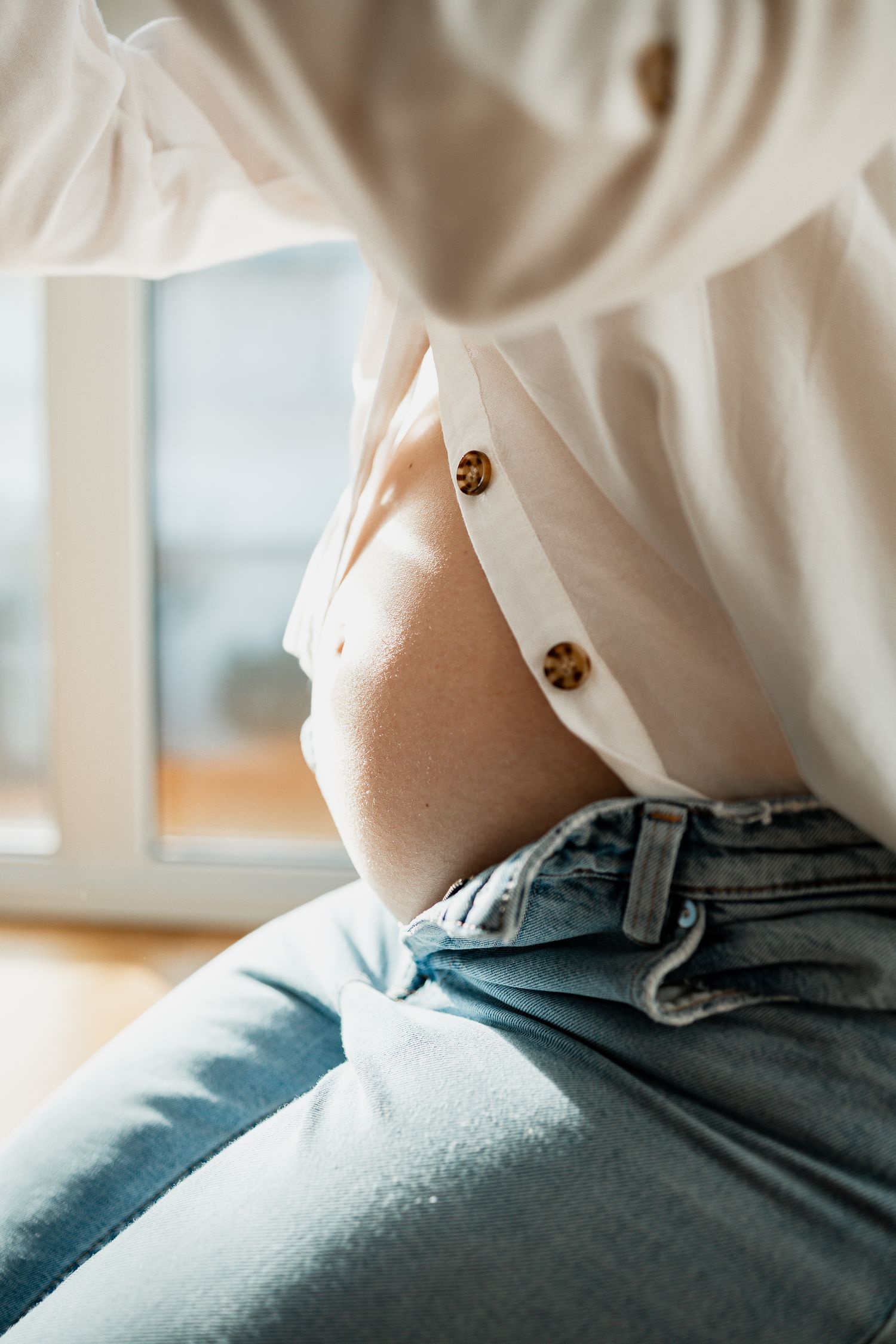 Close-up view of a white button-up shirt and blue jeans against natural lighting from a window.