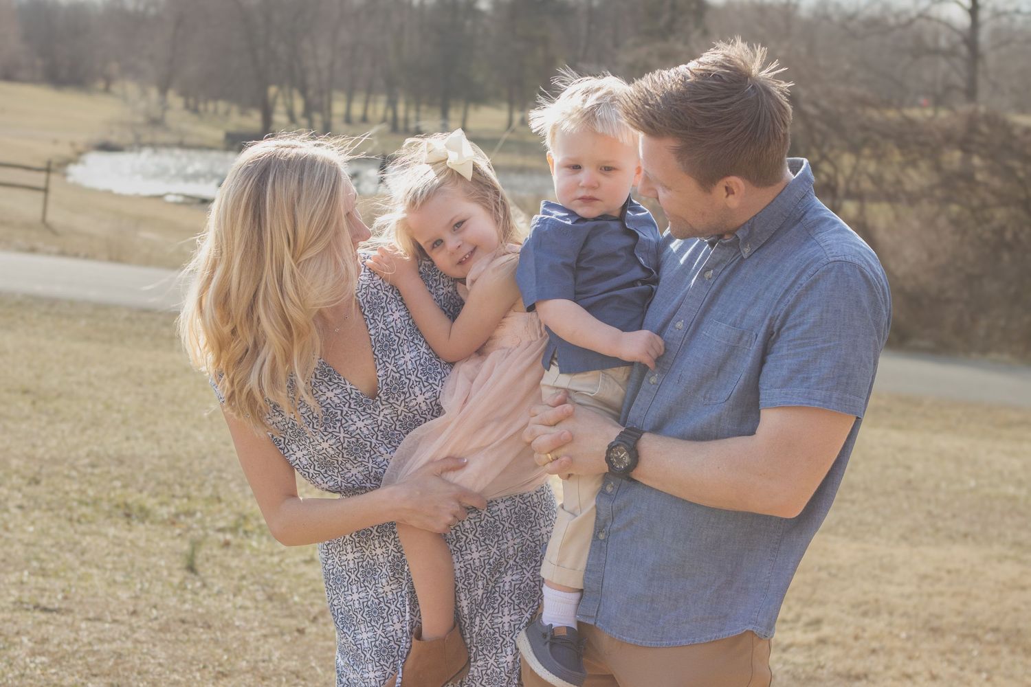 Family enjoying playful moment together in sunlit field.