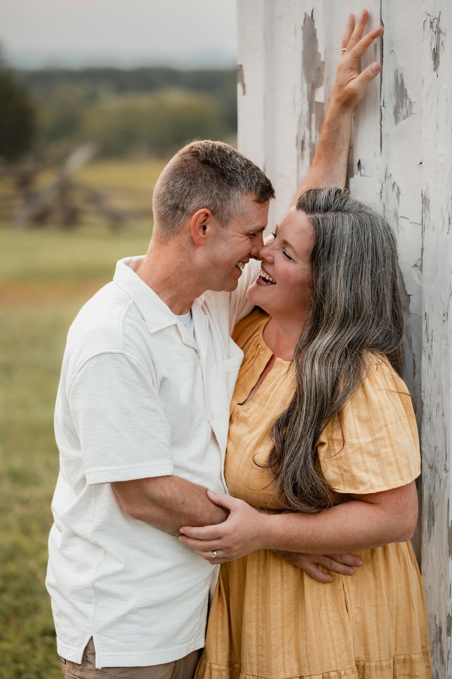 A couple shares a romantic moment leaning against a rustic white barn wall outdoors.