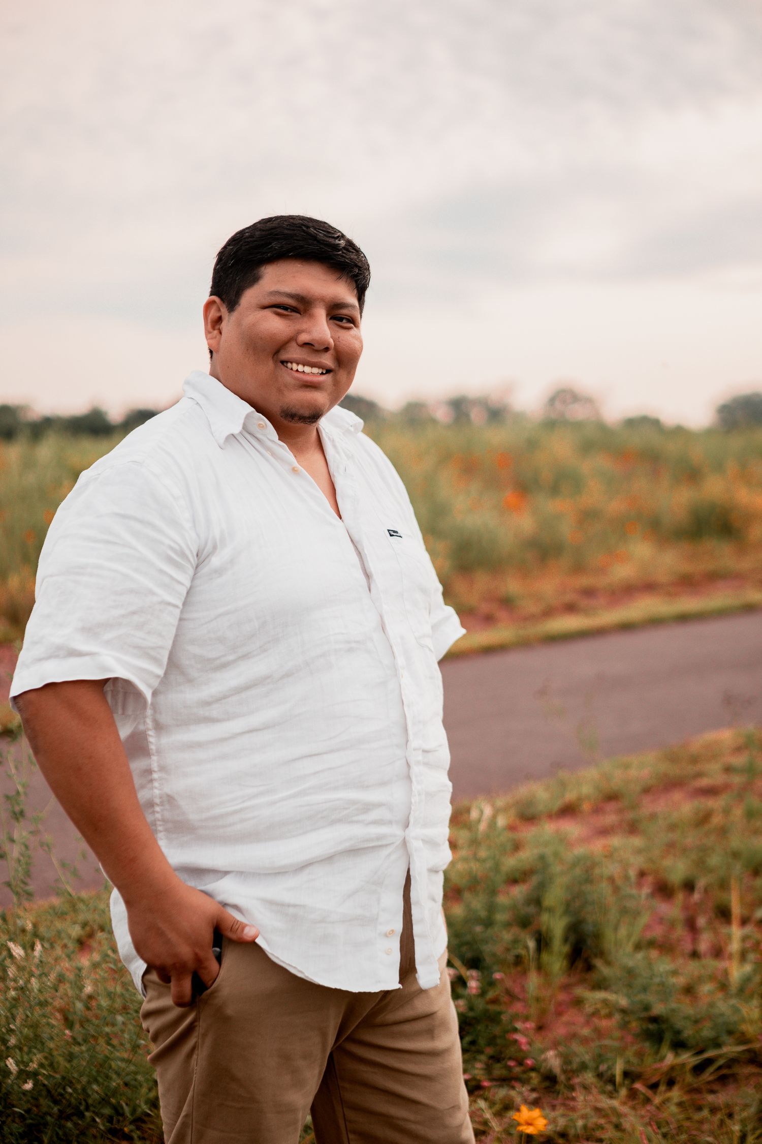 A person wearing a white button-down shirt and khaki pants stands amid a flower garden at sunset.