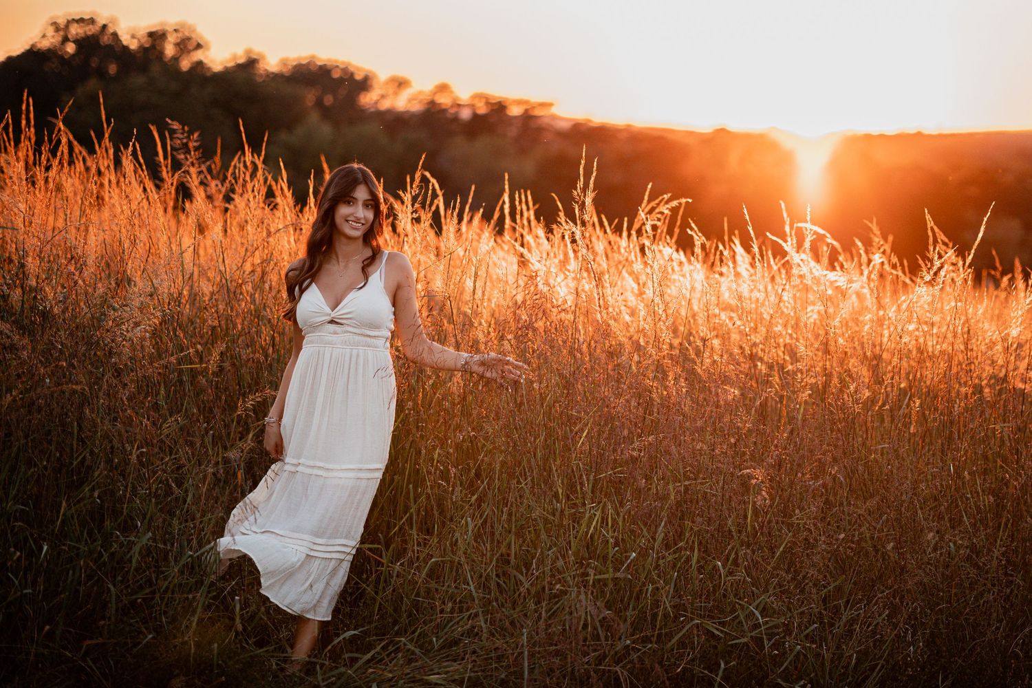 Person in white dress standing among tall golden grass during magical sunset moment.