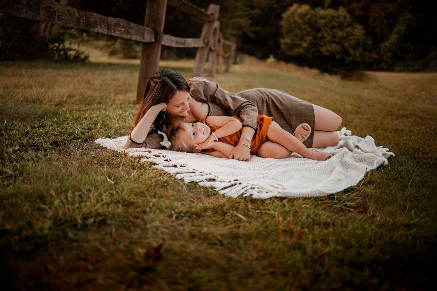 A tender moment shared between two people lying on a white blanket in a grassy field at sunset.