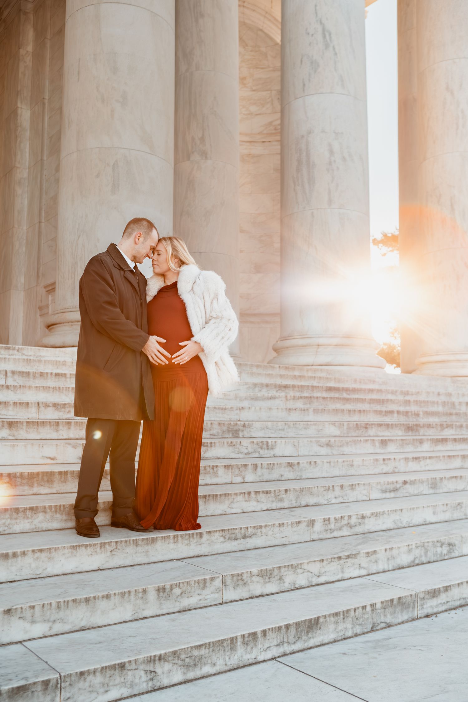 Romantic couple embraces on grand marble steps at sunset with dramatic columns and warm lighting in background.