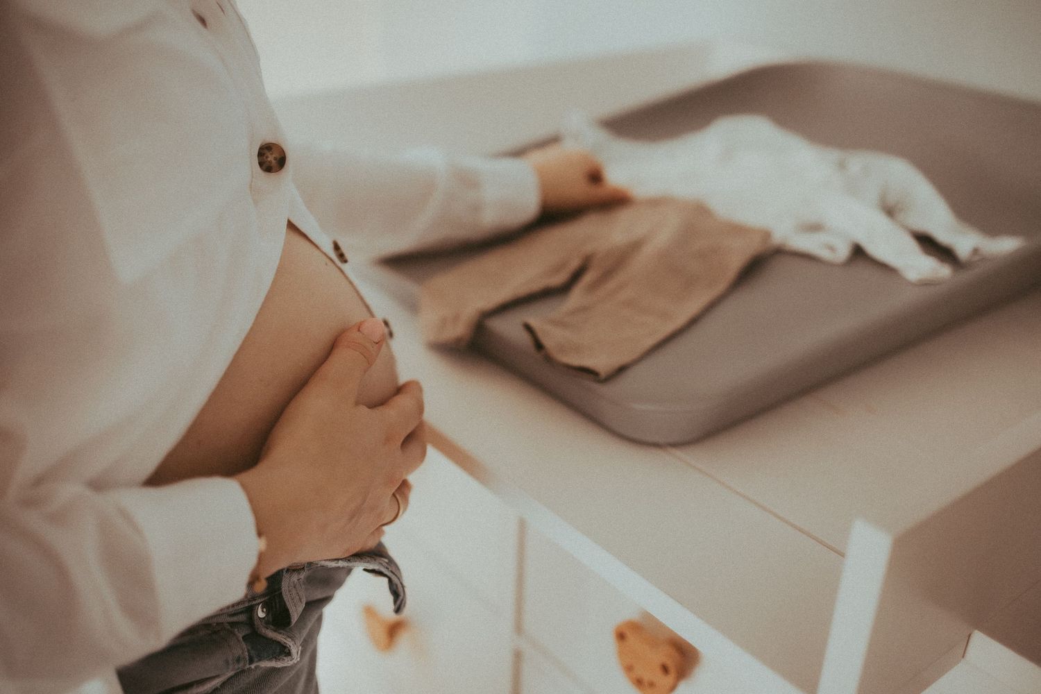 Chef in white uniform buttons up jacket while standing in professional kitchen with utensils and equipment nearby.