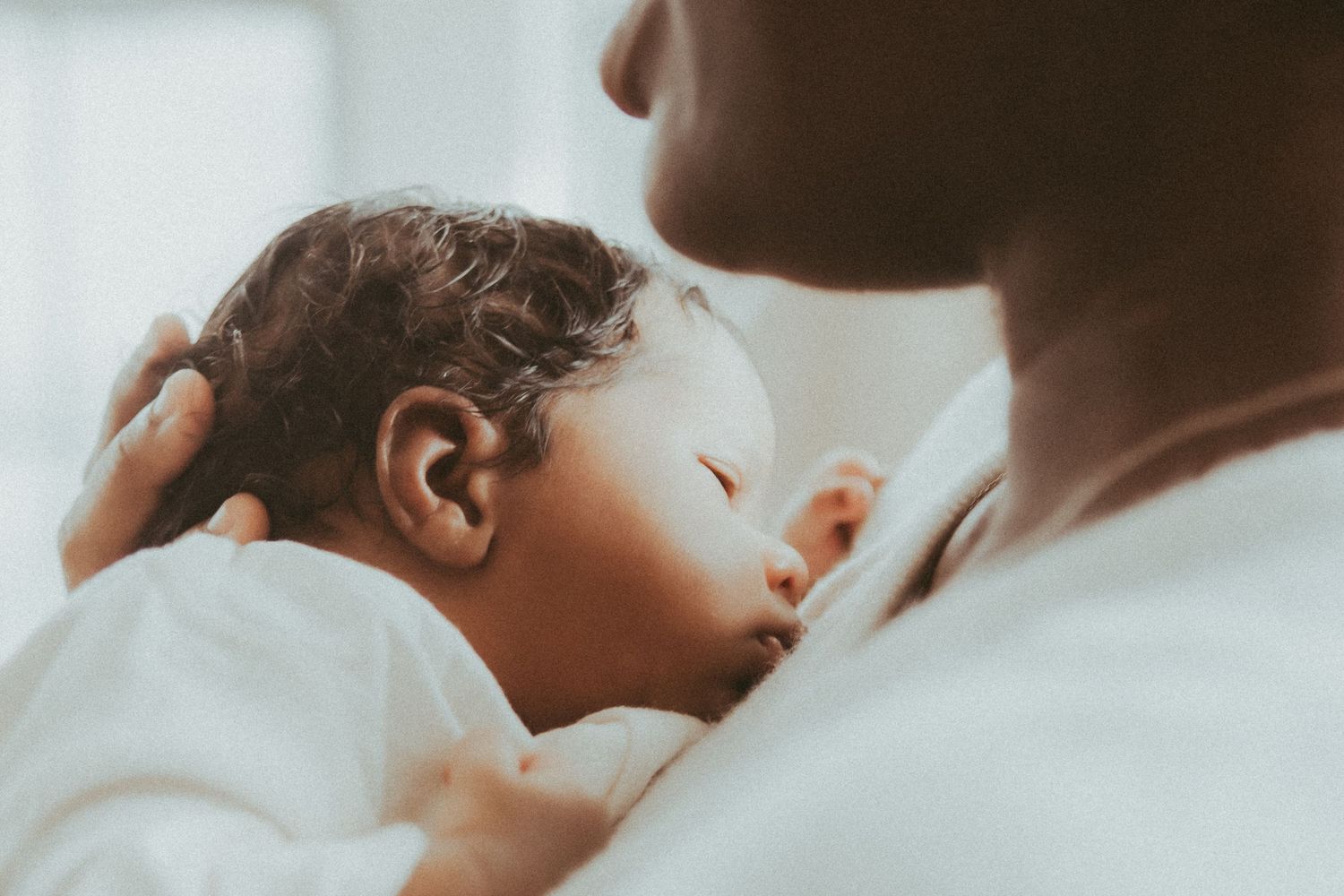 A tender moment between parent and sleeping baby in soft, dreamy lighting.