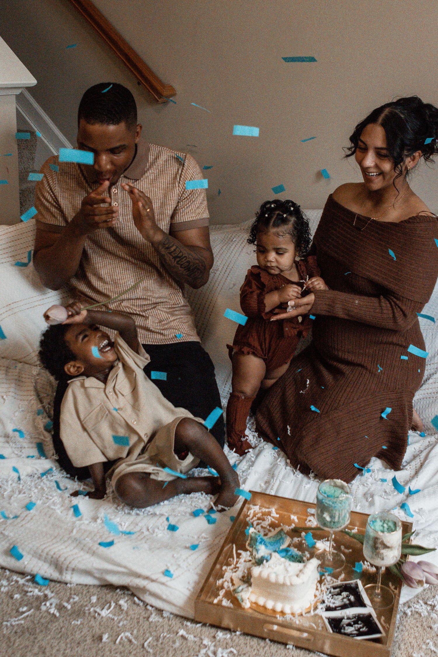 A gender reveal celebration with blue confetti and ultrasound photos shows a family's joyful reaction on a couch.