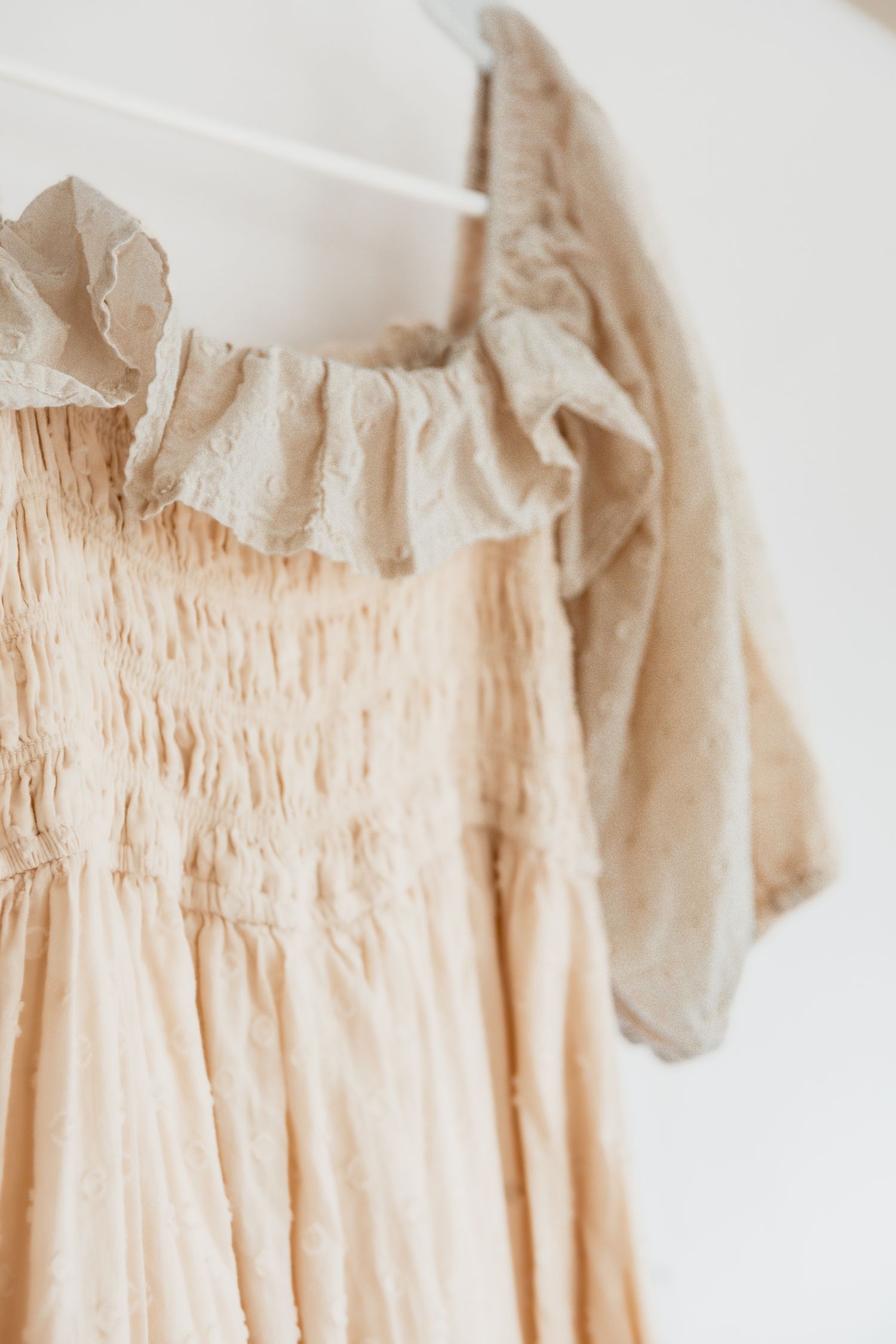 Close-up details of a cream colored vintage dress with delicate ruffles and smocking details at the neckline.
