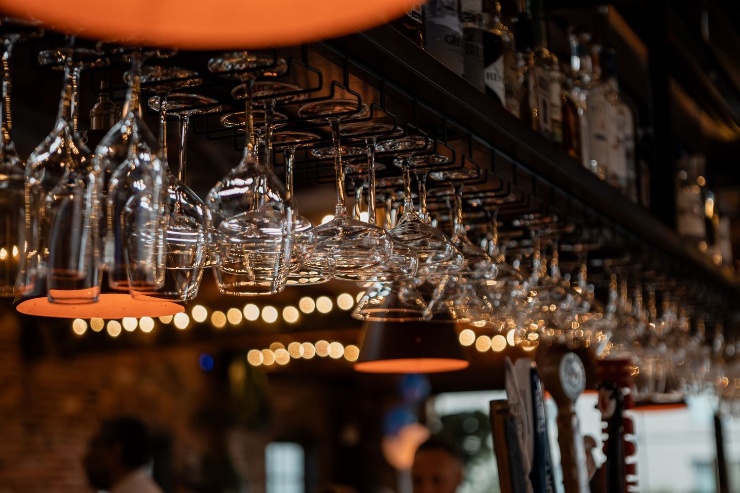 Wine glasses hang upside down from a rustic wooden ceiling rack illuminated by warm pendant lighting.