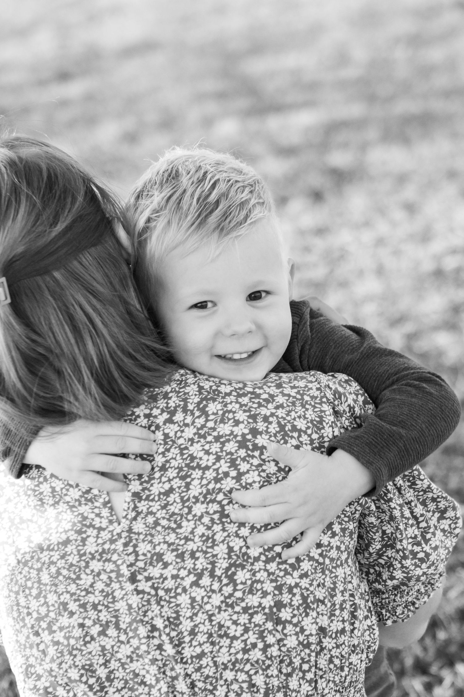 Black and white photo of a joyful embrace between child and adult wearing floral print.