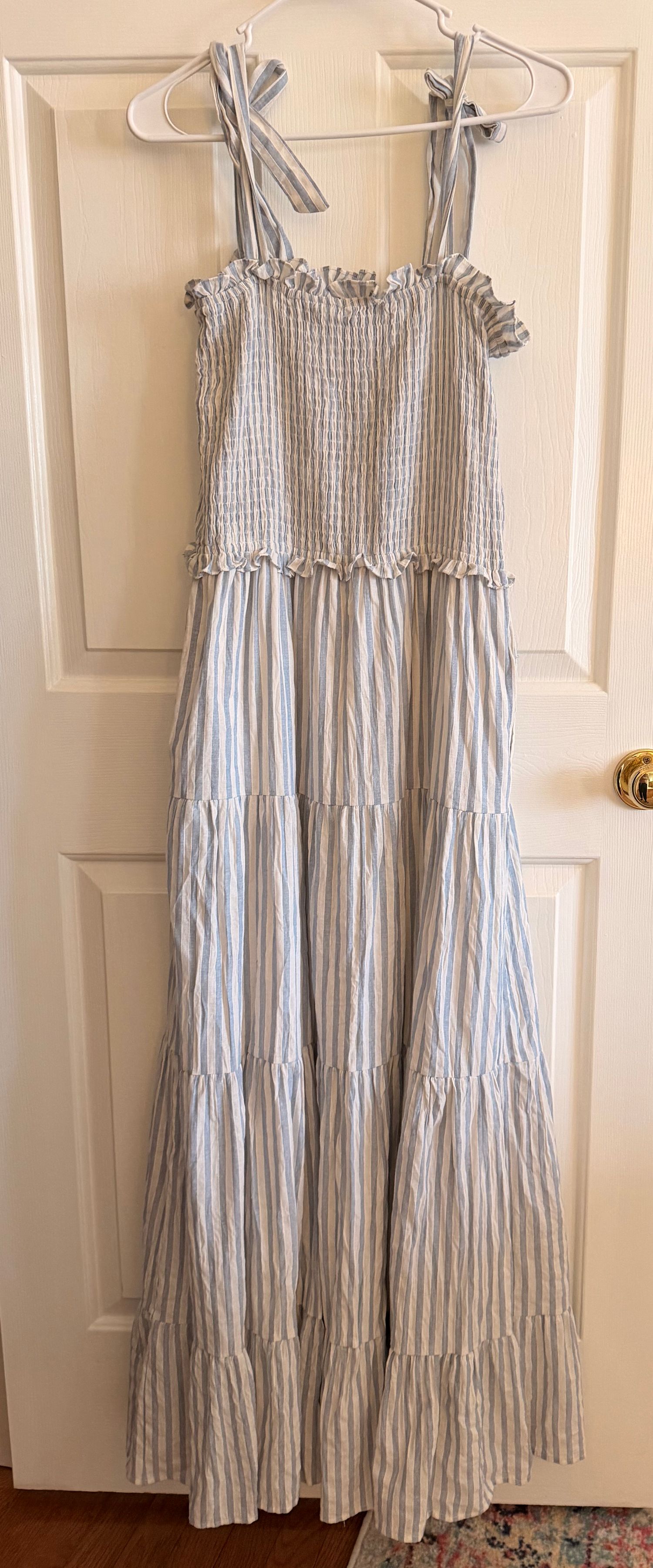 Light blue and white striped sundress with smocked bodice and tiered ruffle skirt hanging on white hangers.