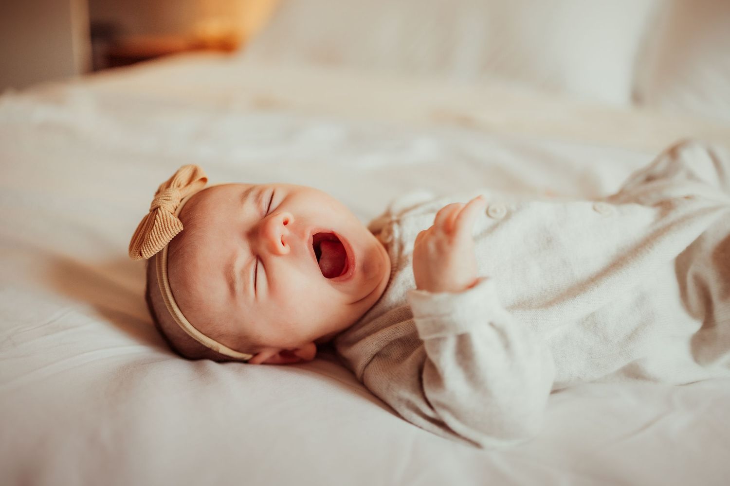 A newborn baby yawns while lying on soft white bedding in a series of connected photos.