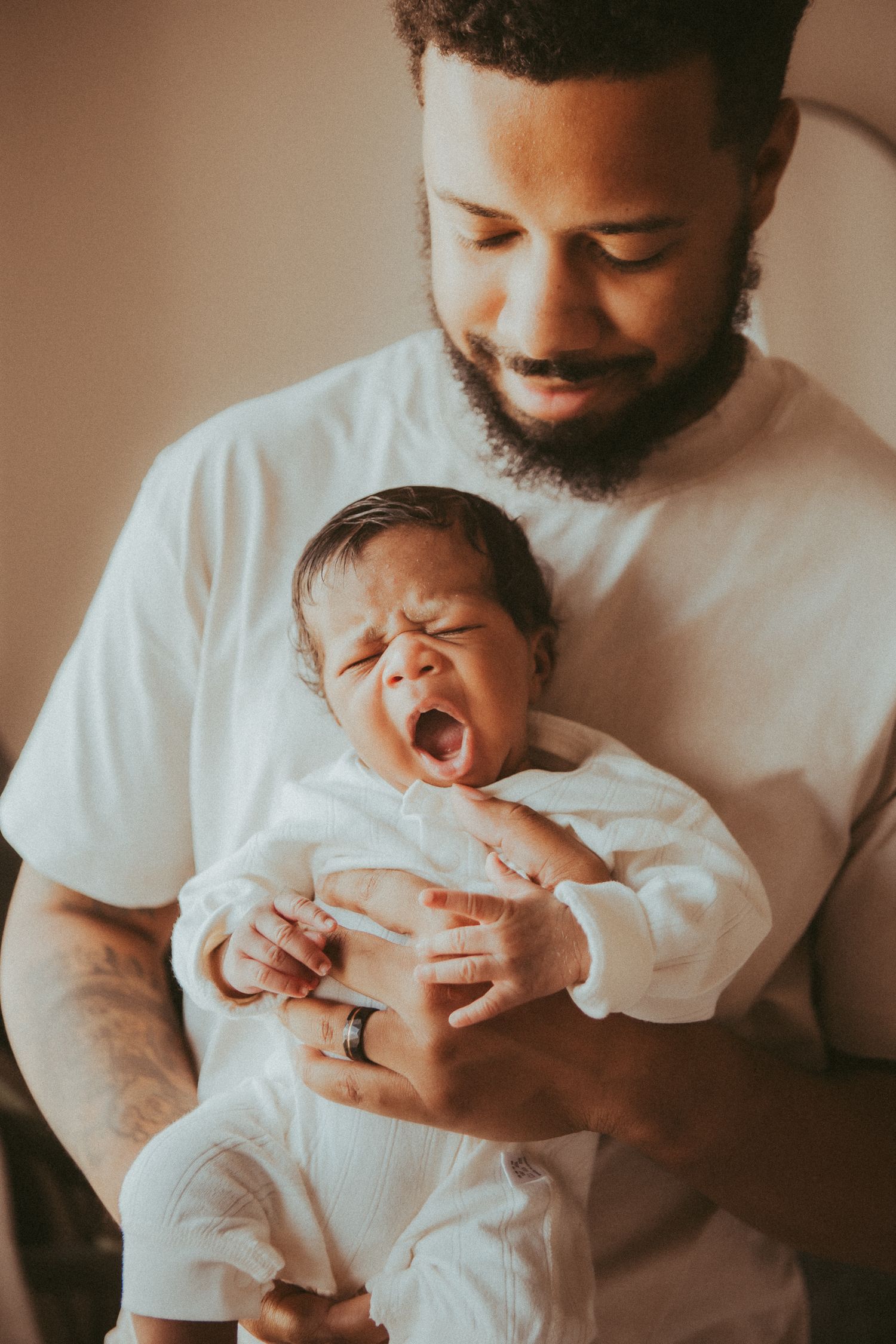 Parent holding and comforting their yawning newborn baby while wearing a white t-shirt.