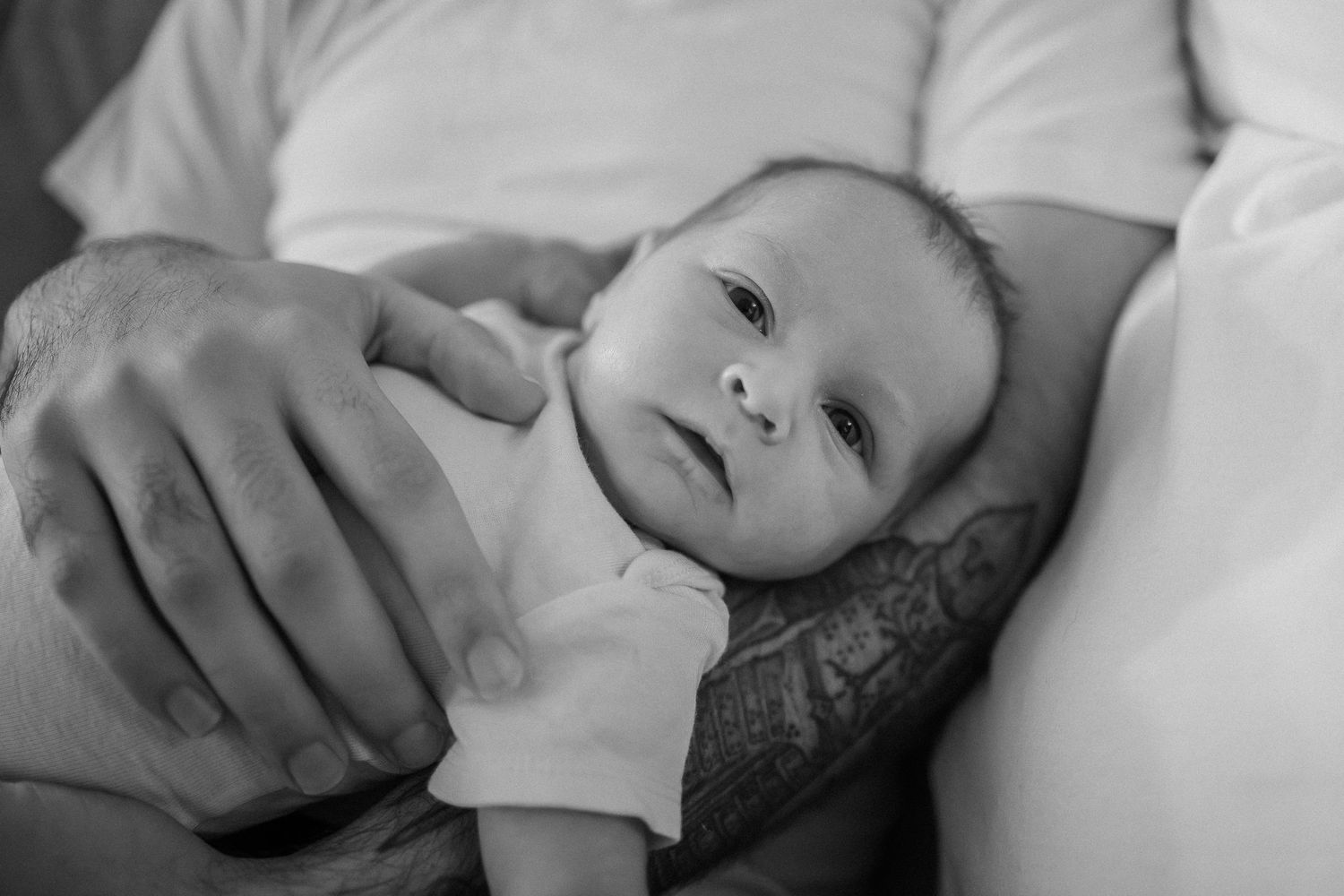 Black and white photo collage of a baby lying on white bedding showing different facial expressions and poses.