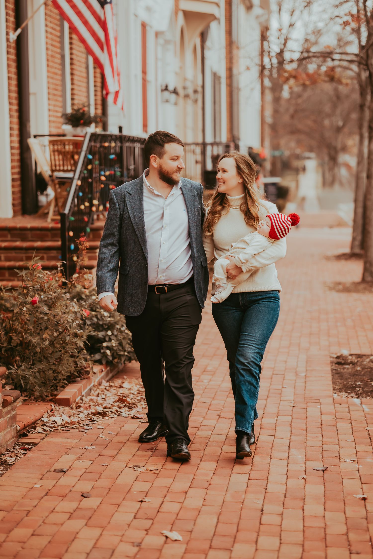 Family strolls together on brick sidewalk with American flag and holiday decorations visible.