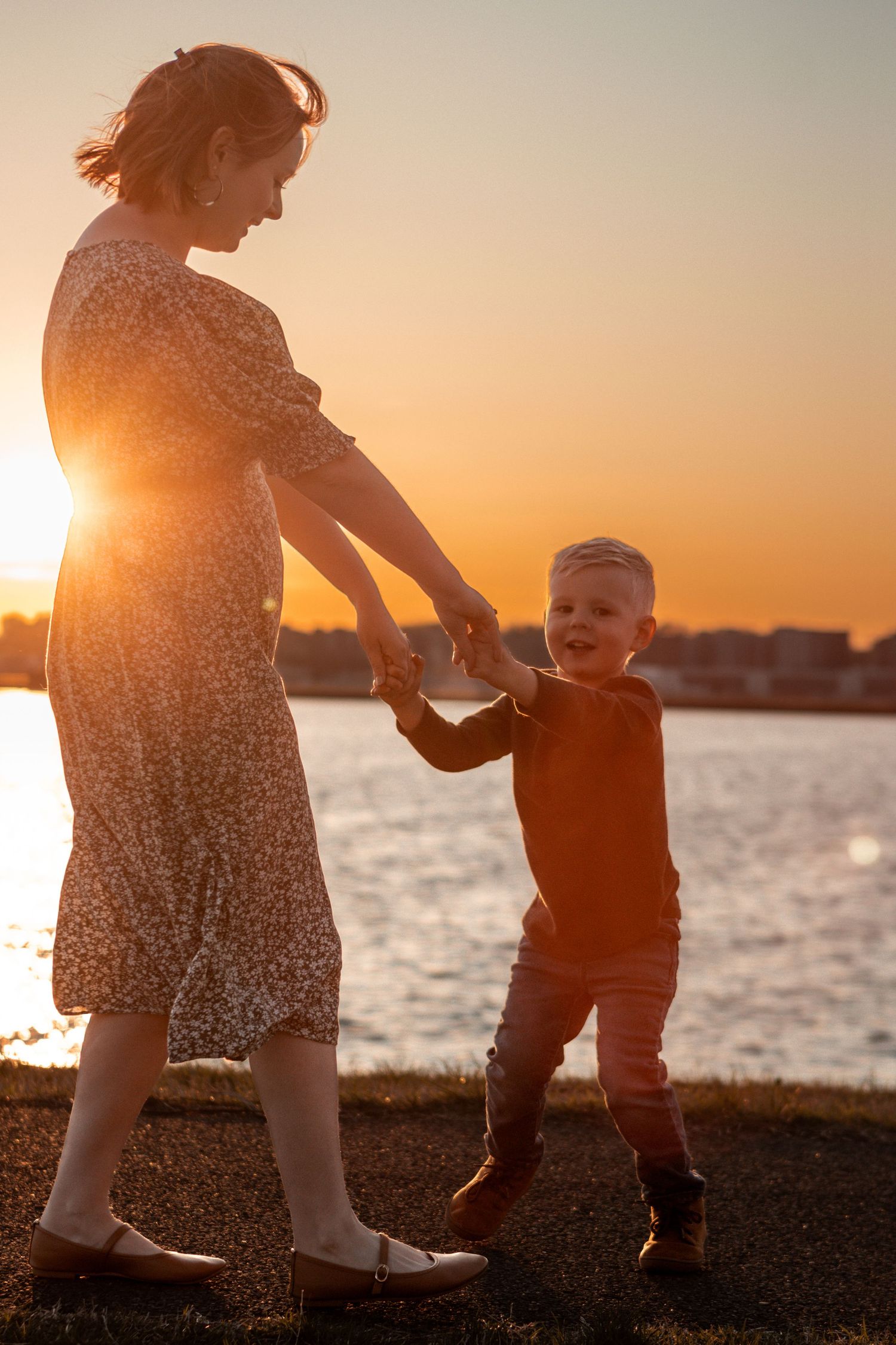 Golden sunset silhouettes against the water as family plays on grassy shore.