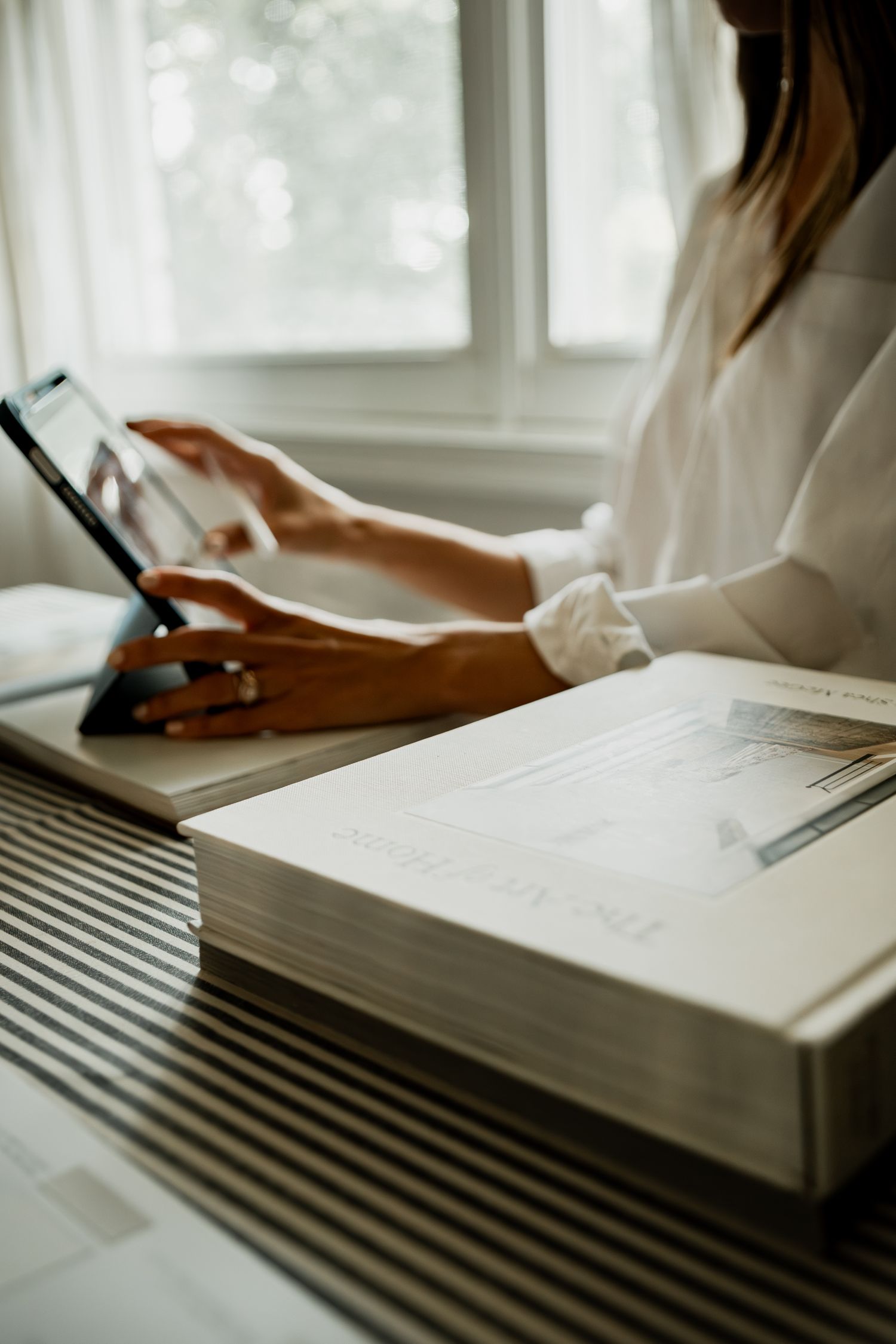 Person studying at desk with open textbook while using digital tablet in soft natural window light.