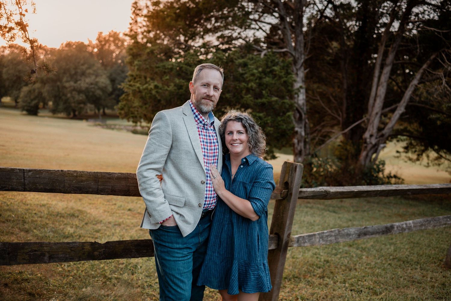 A couple embraces during a romantic outdoor photoshoot at sunset in a scenic park setting.