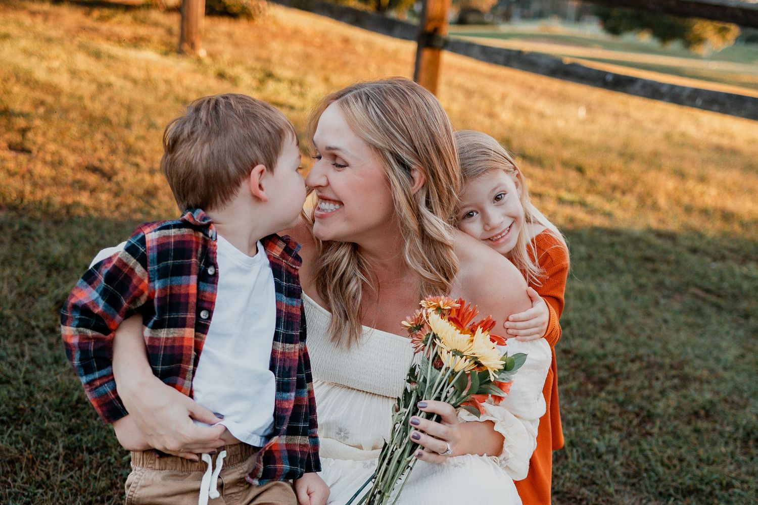 A tender outdoor family moment at sunset with flowers and warm autumn lighting in a grassy field.
