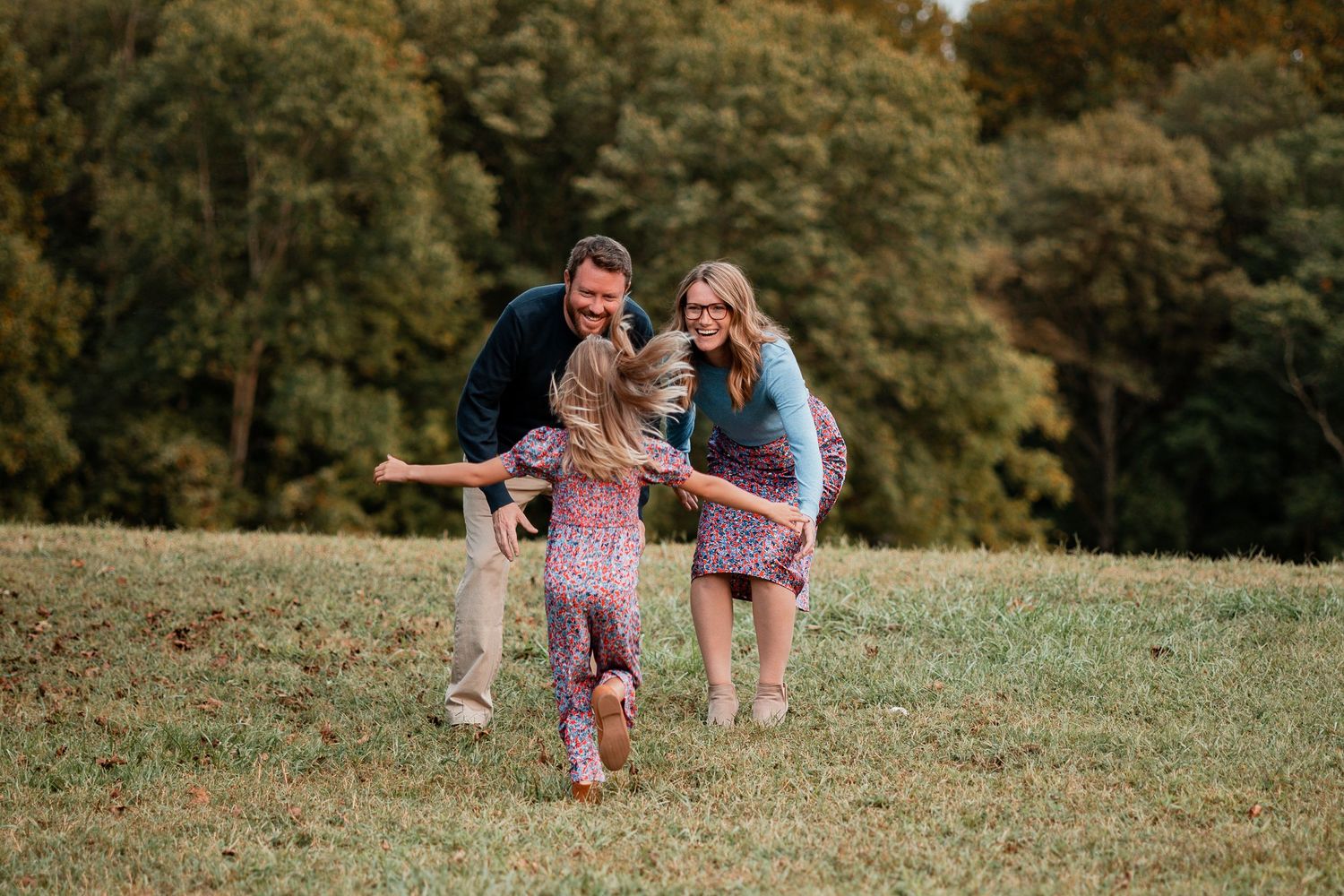 Family running and playing together in a grassy field on an autumn day.