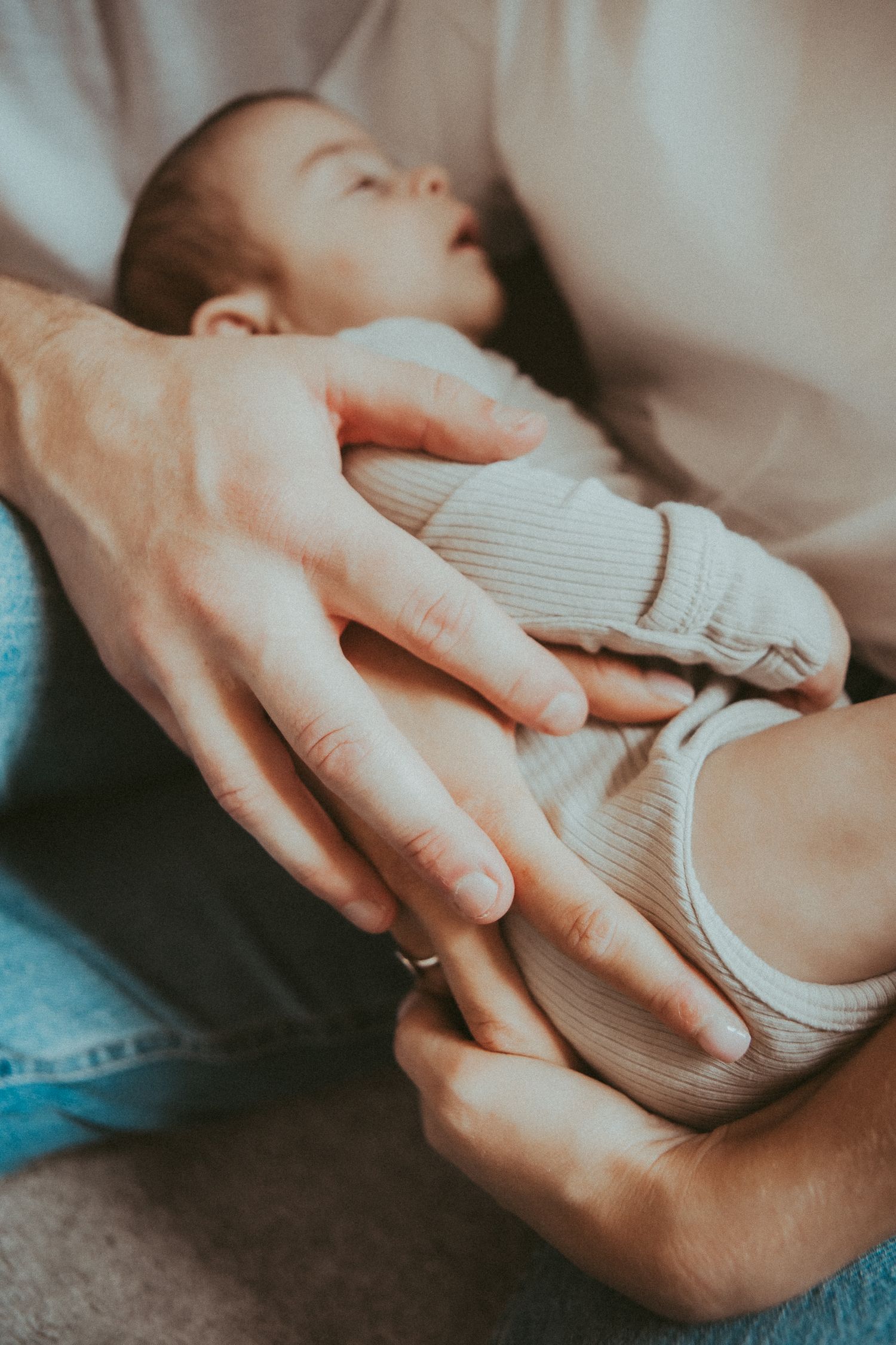 Close-up of gentle hands cradling a baby wearing a ribbed onesie.