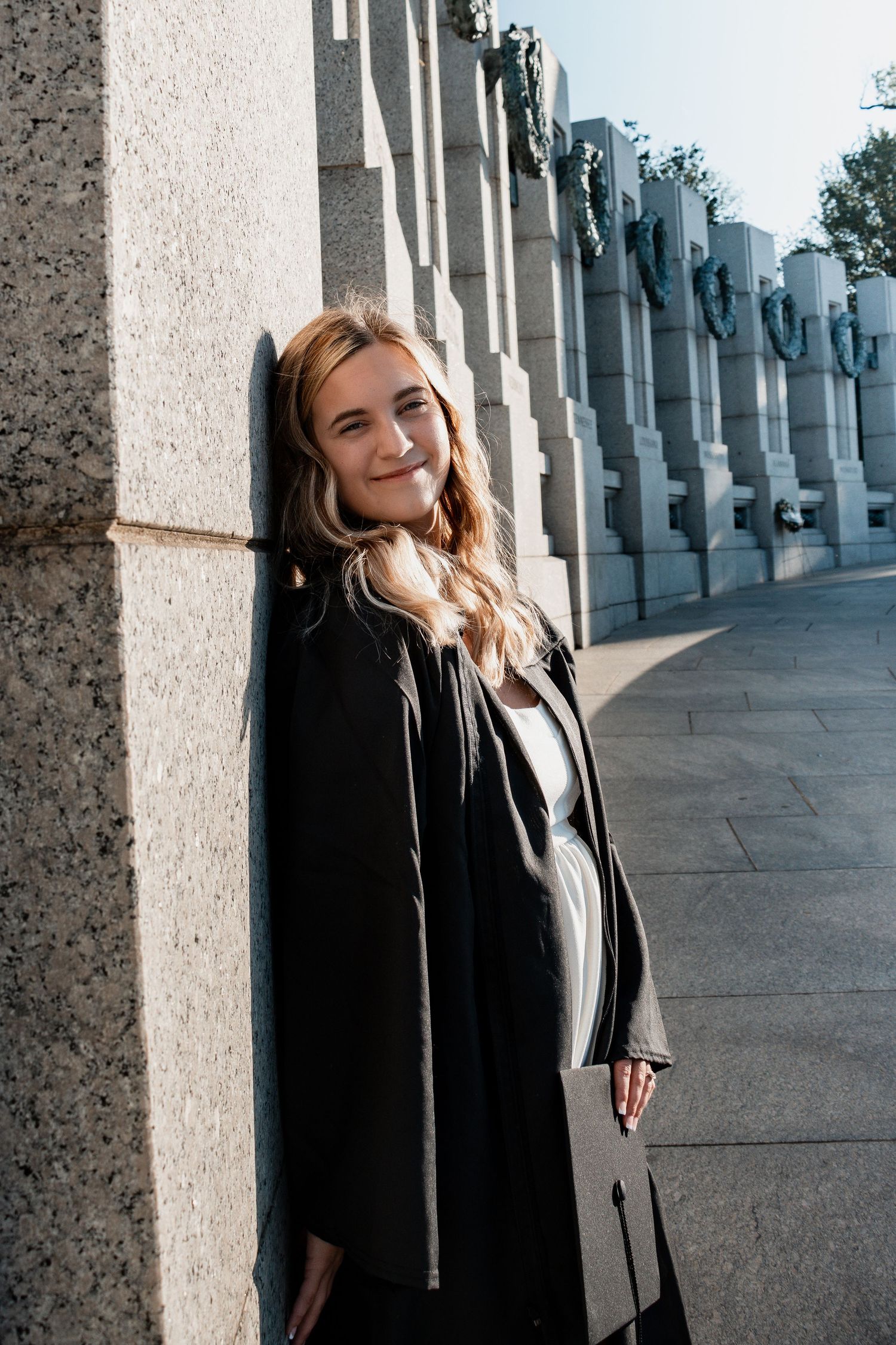 Graduate in formal attire poses elegantly against stone columns at the World War II Memorial in Washington DC.