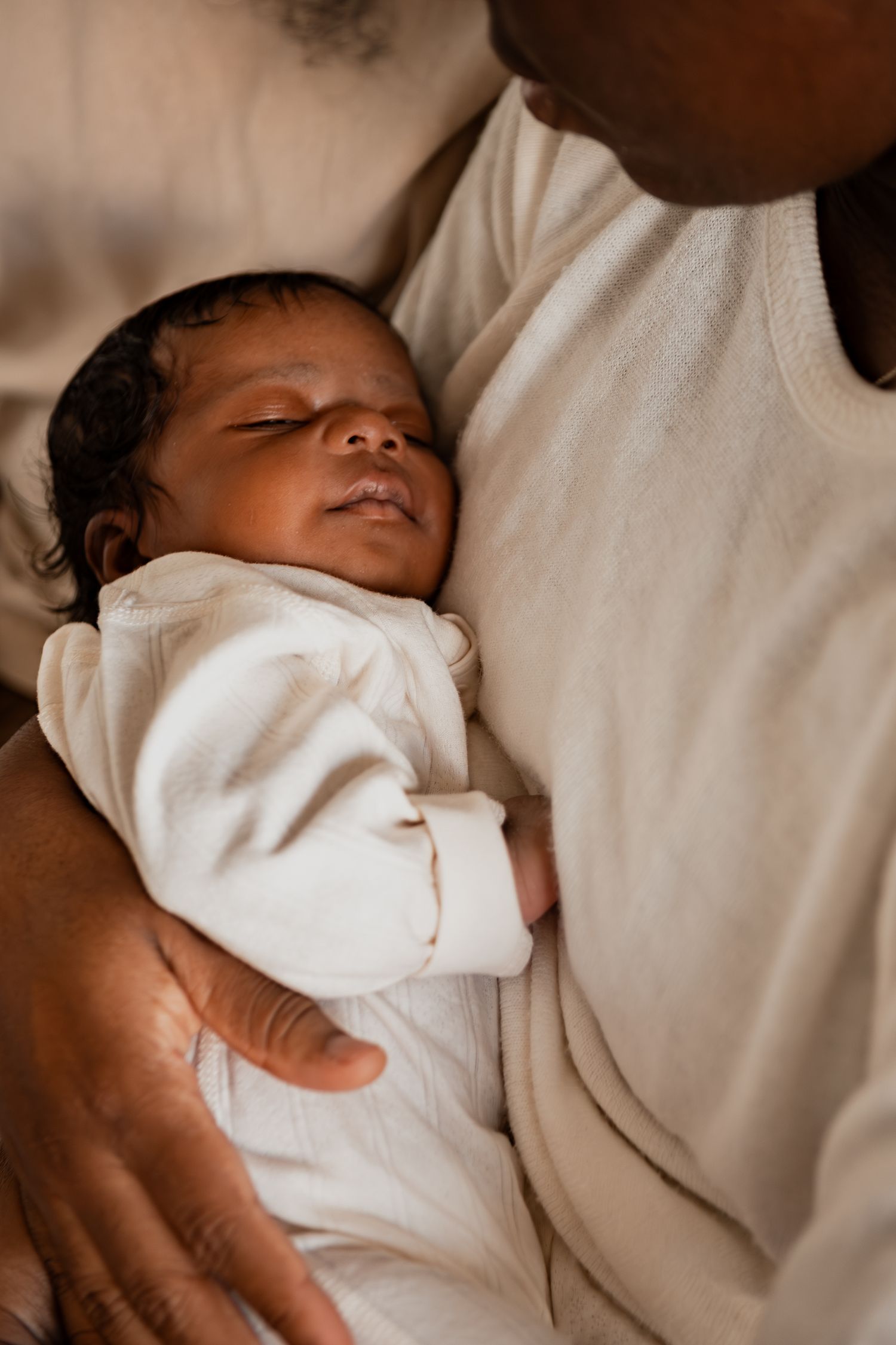 Peaceful newborn baby sleeping soundly while cradled in white blankets against a neutral background.