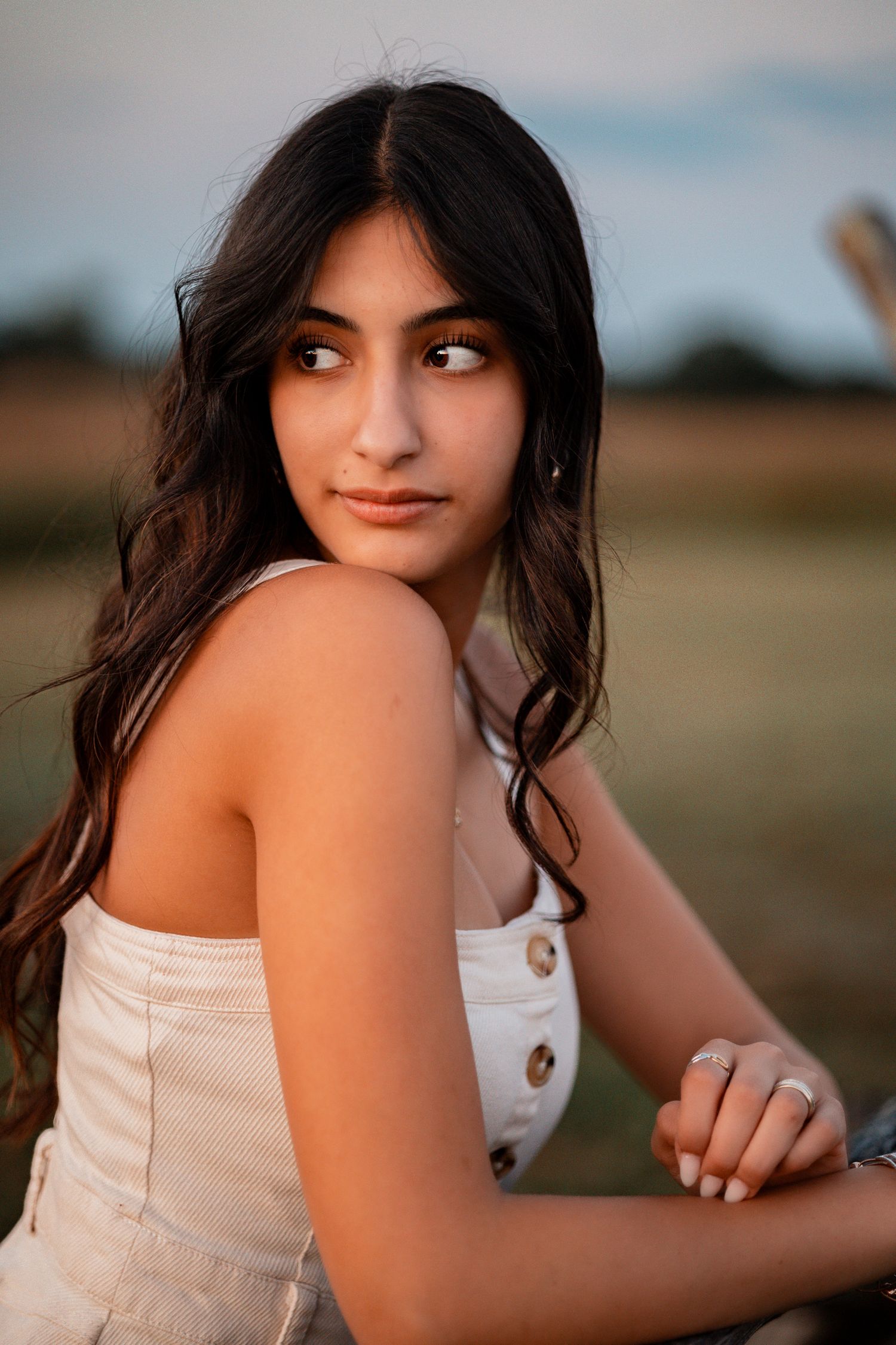 Close up shot in white summer dress against blurred natural background at sunset.