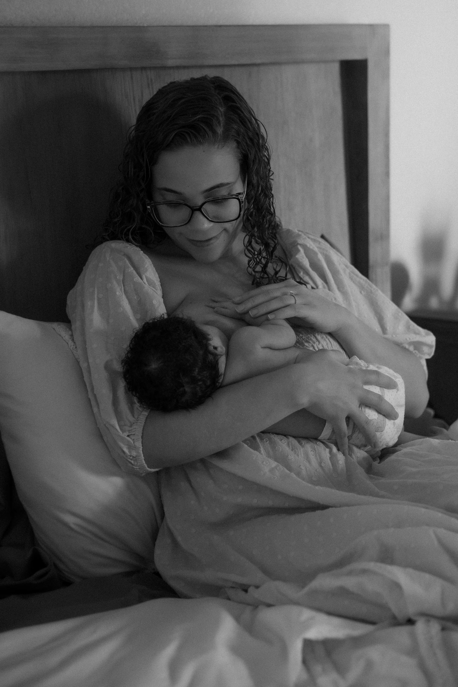 Mother breastfeeding newborn baby while sitting in bed, black and white portrait photo.