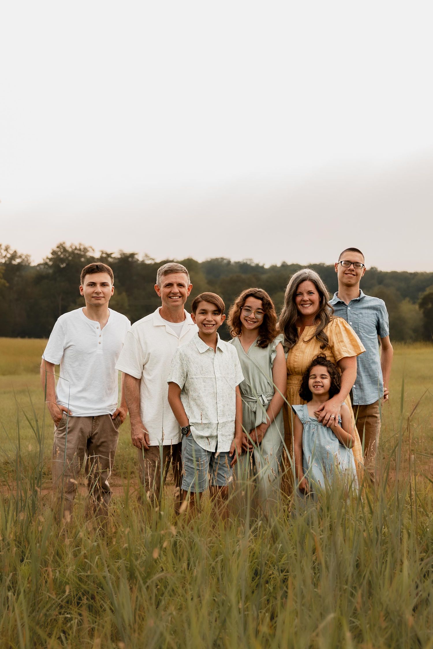 A joyful family of seven poses together in a lush green field during golden hour.