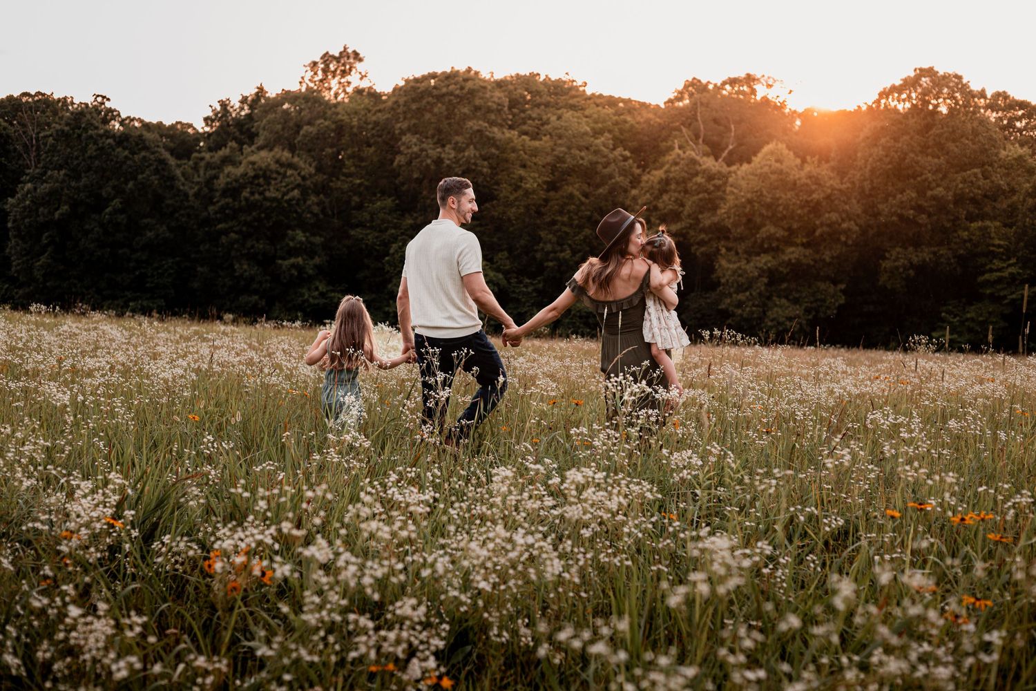 Family walking together through a golden wildflower meadow at sunset during a summer photo session.