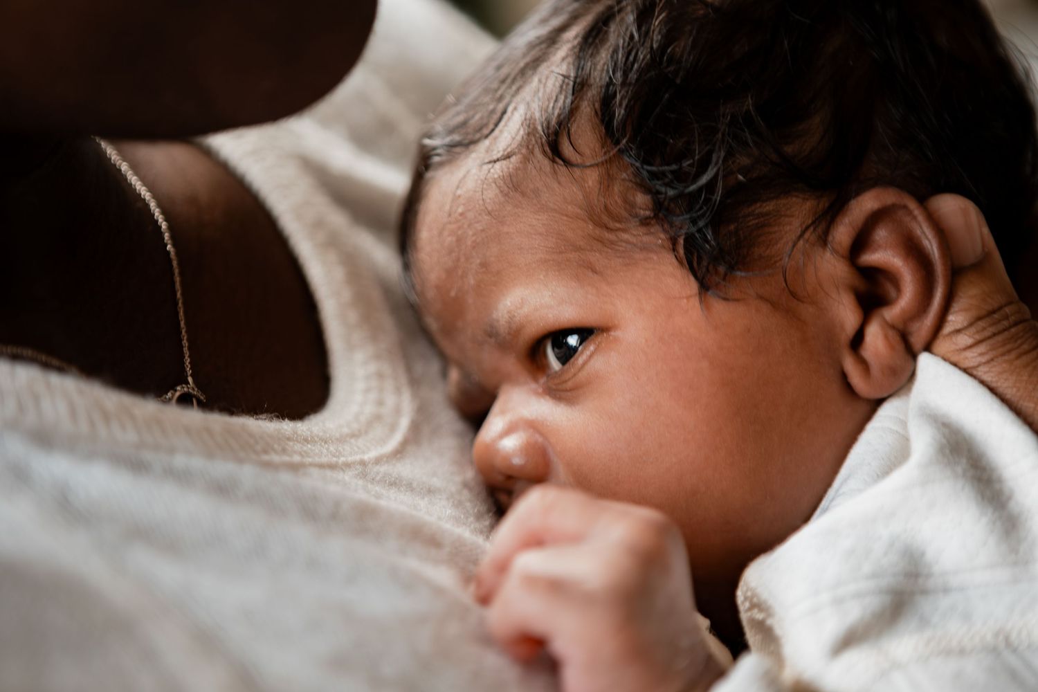 Parent cradling a sleeping newborn baby against their chest in an intimate bonding moment.