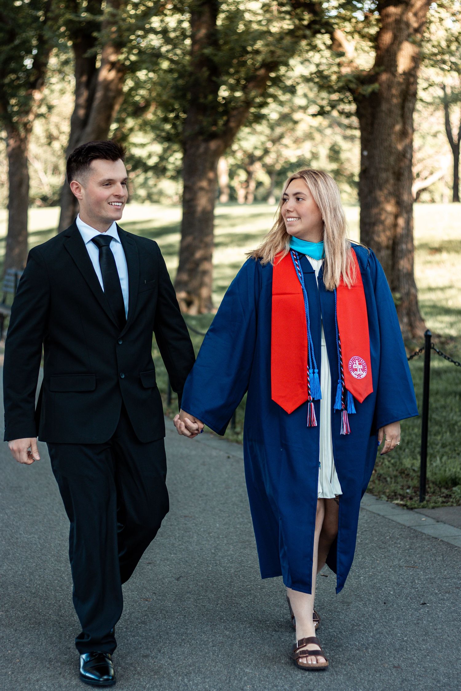 Graduates walking together on a path surrounded by trees in commencement attire.