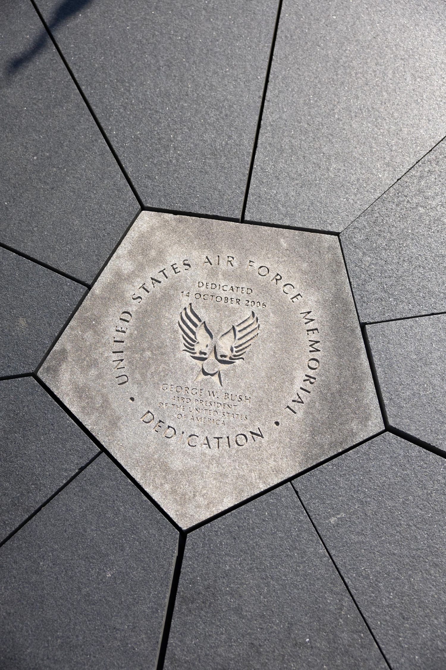 Bronze pentagon dedication plaque for the United States Air Force Memorial, dedicated October 2006, set in dark stone pavement.