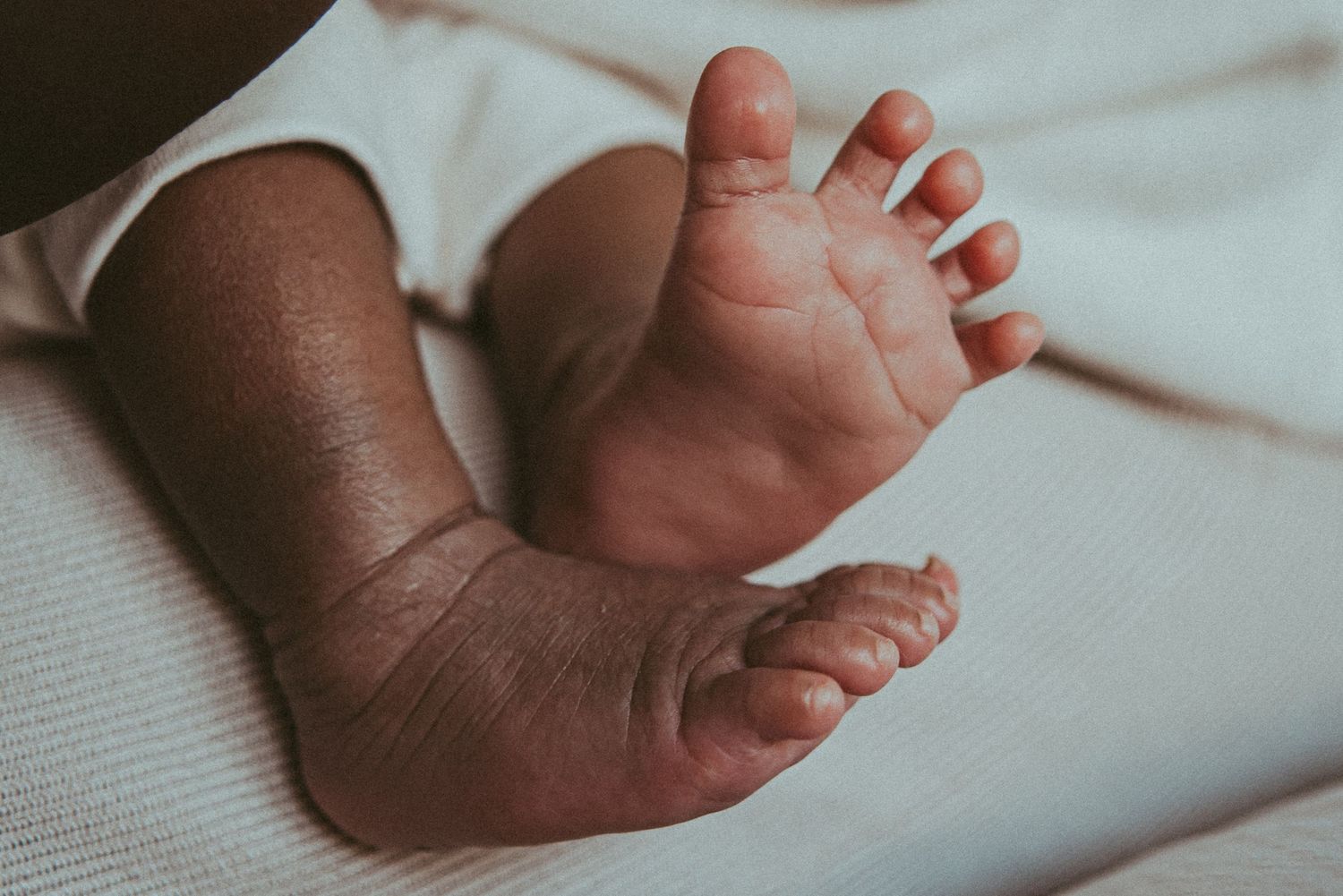 Close-up view of tiny newborn baby feet against white fabric background.