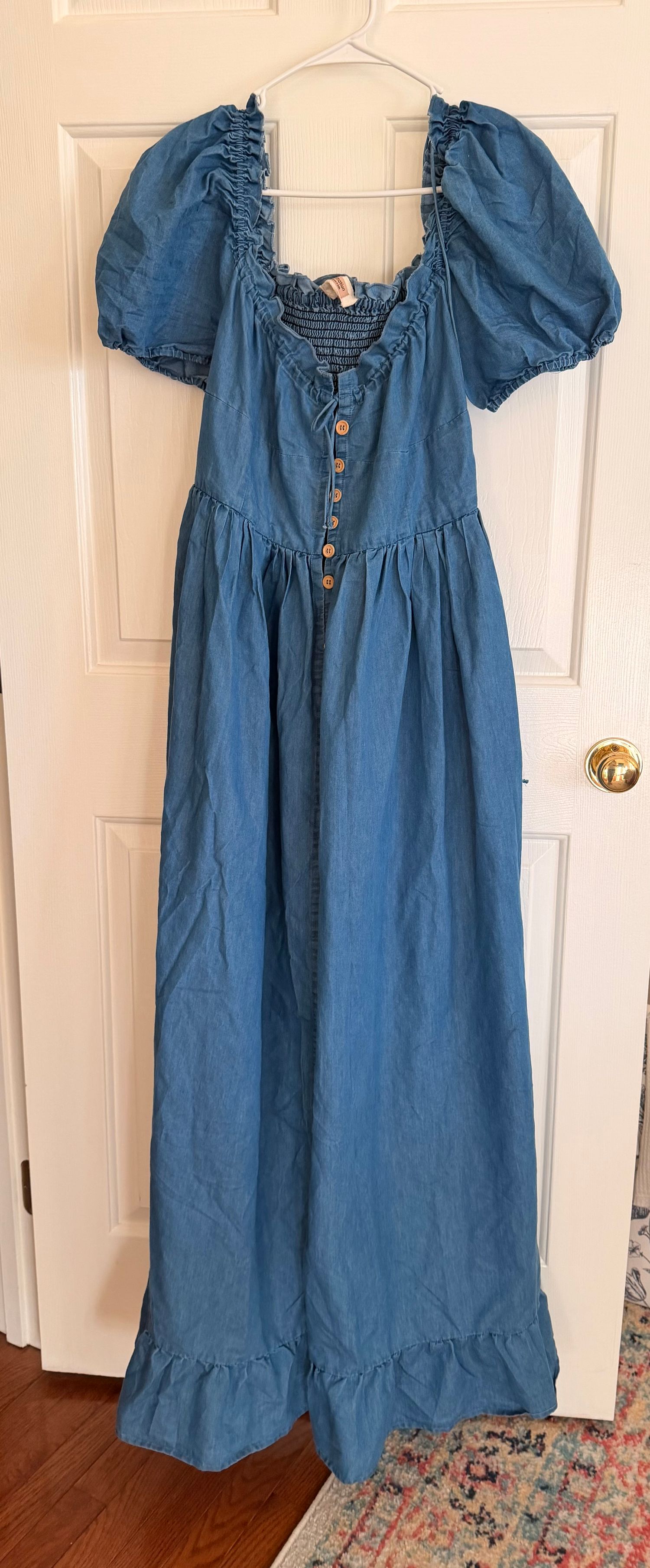 Vintage-style denim maxi dress with puff sleeves, button front, and ruched bodice hanging on white door.