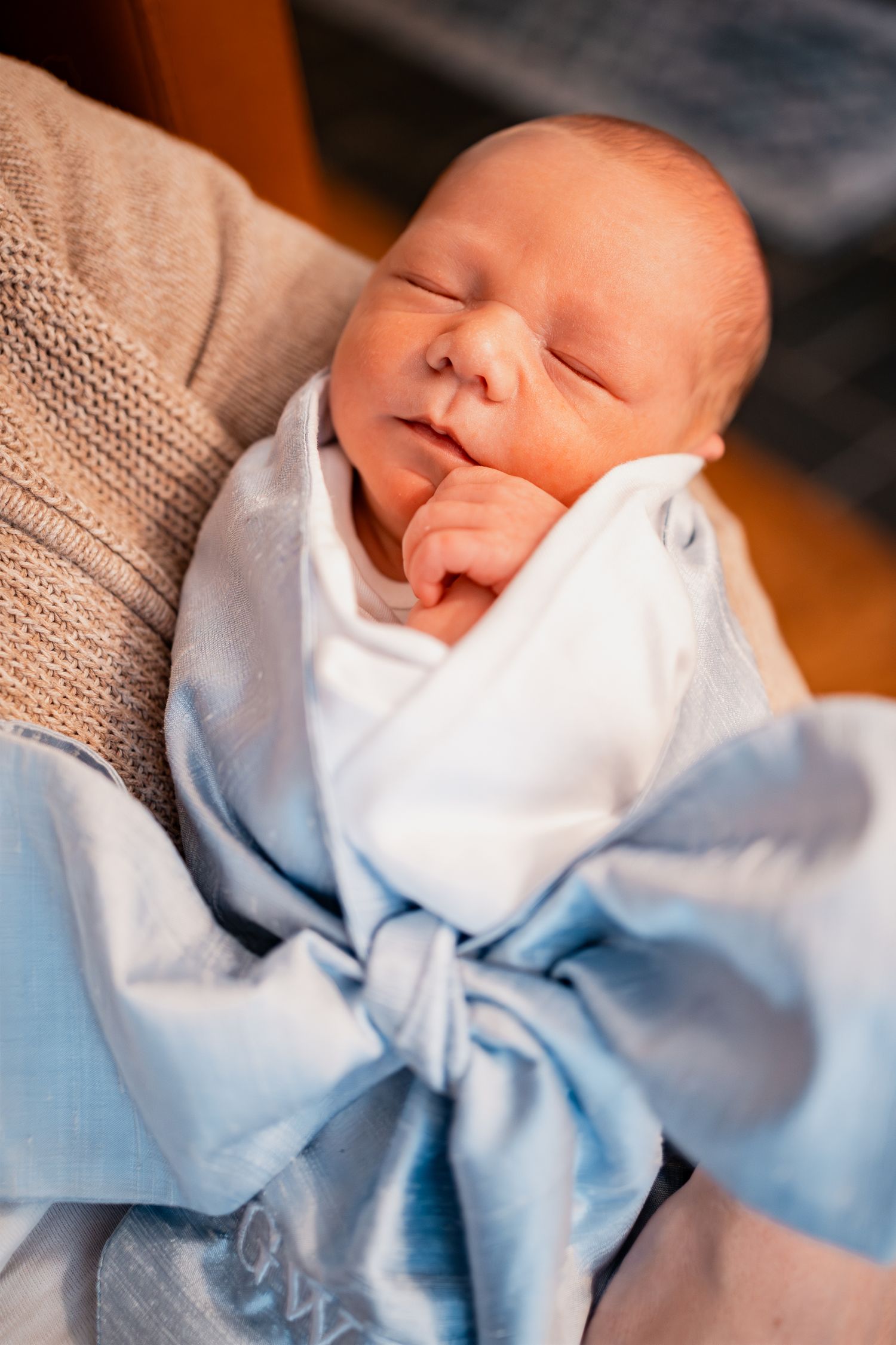 Newborn baby wearing a light blue bow tie and white outfit resting peacefully.