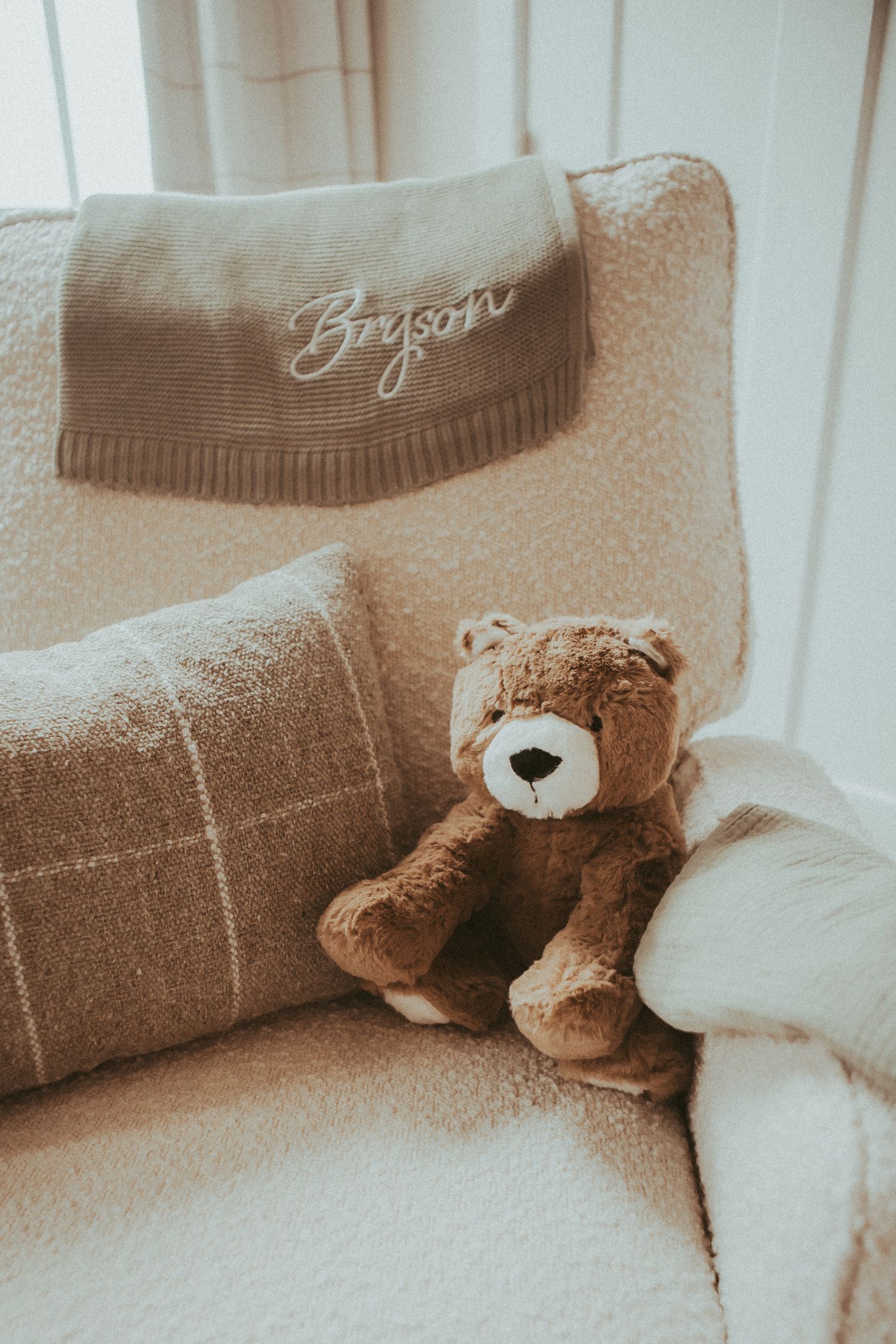 Cozy nursery scene with brown teddy bears and plush pillows arranged on neutral bedding.