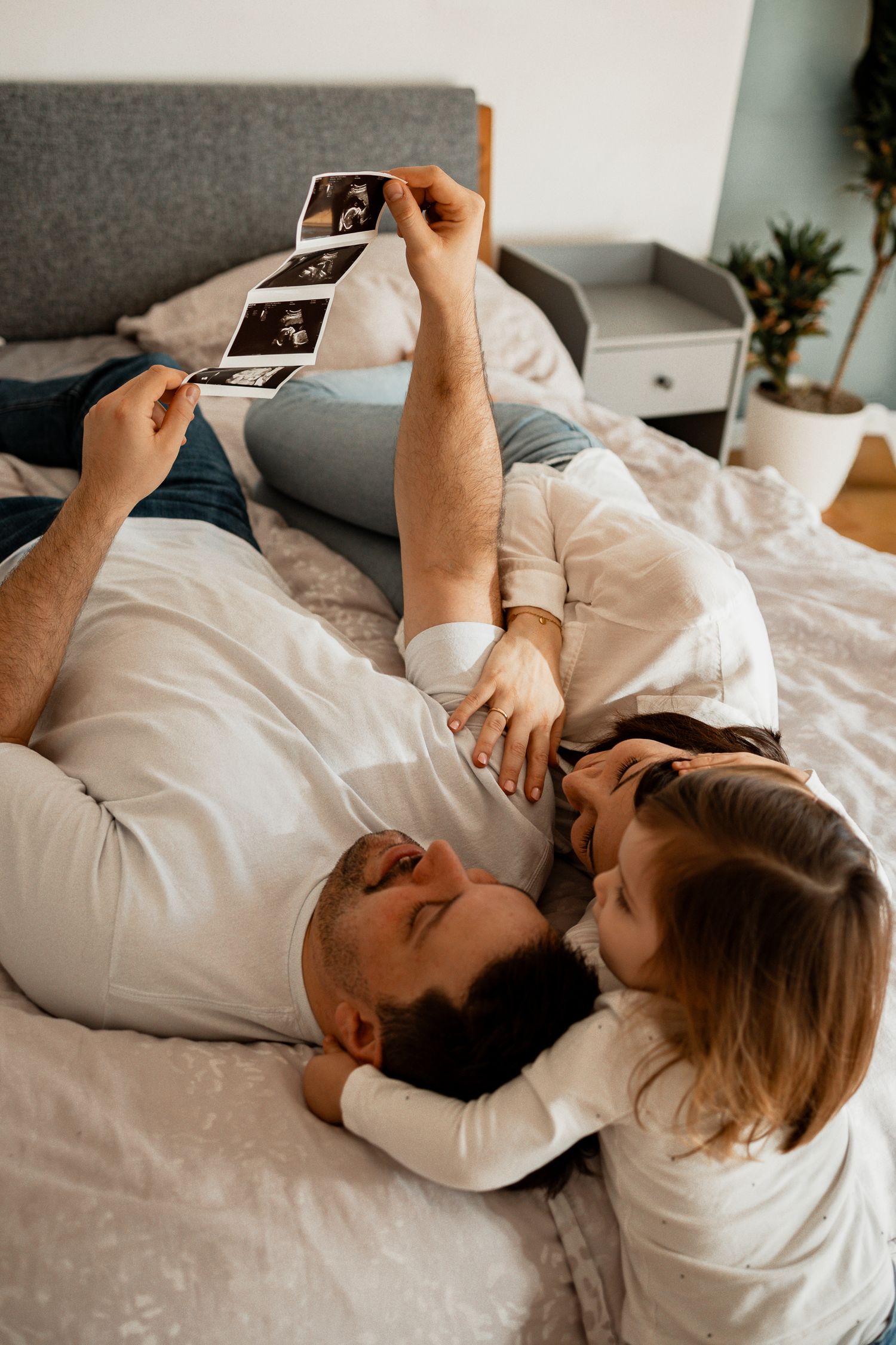 A couple lying in bed together looking at ultrasound photos in a series of intimate moments.