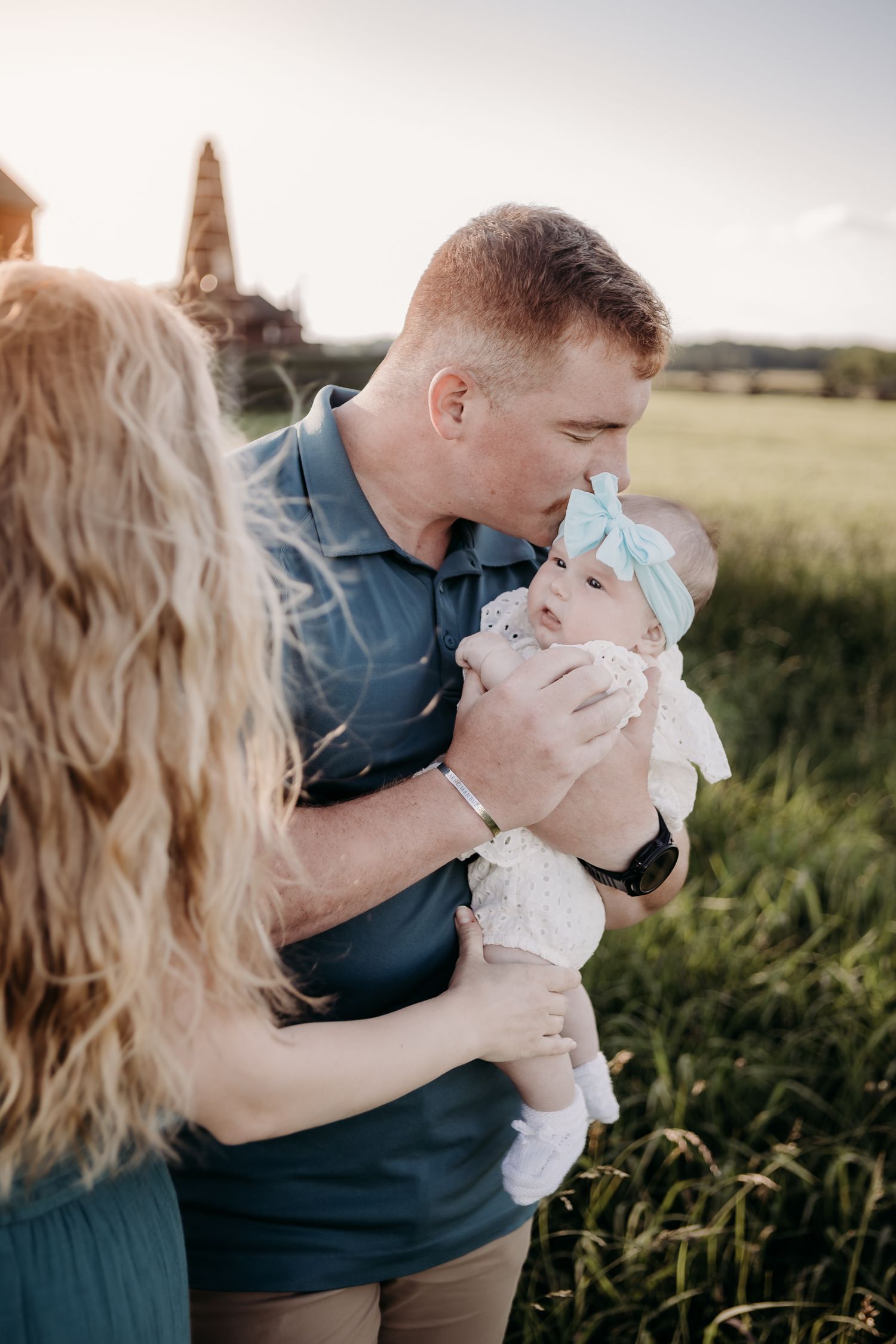 Parents share tender moments with their infant outdoors in a golden field at sunset.