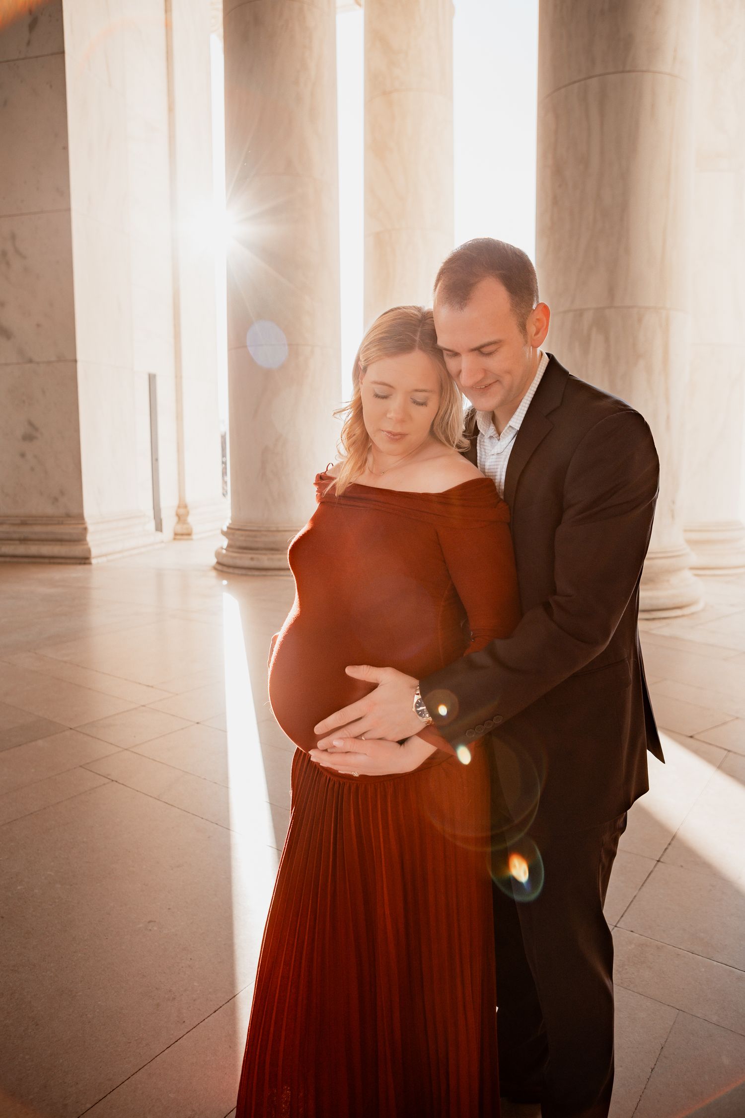 A couple shares an intimate dance moment in an elegant columned hall filled with soft, warm light.