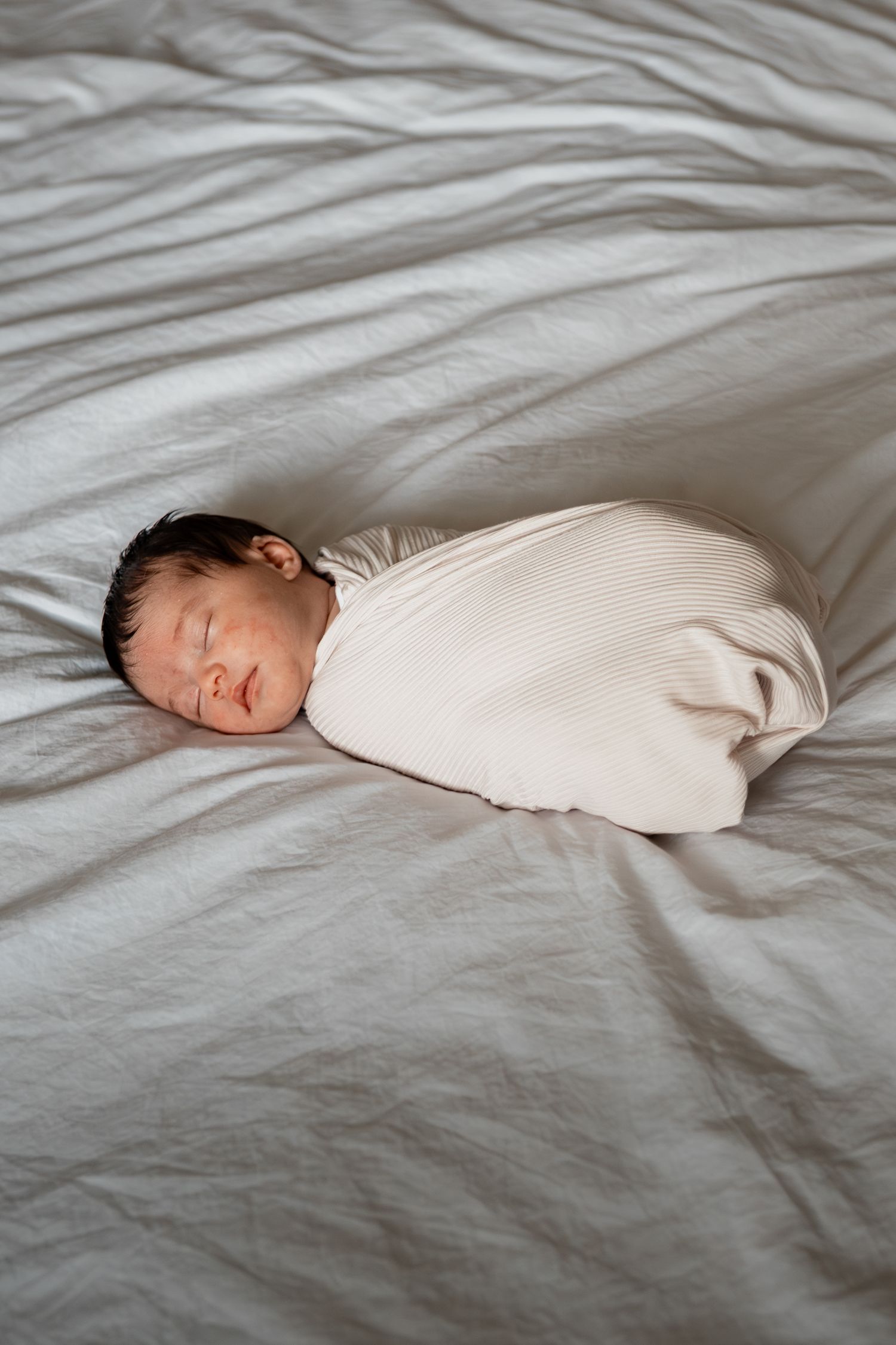 A sleeping baby wrapped in white cloth lies on wrinkled grey bedding, shown in a series of peaceful positions.