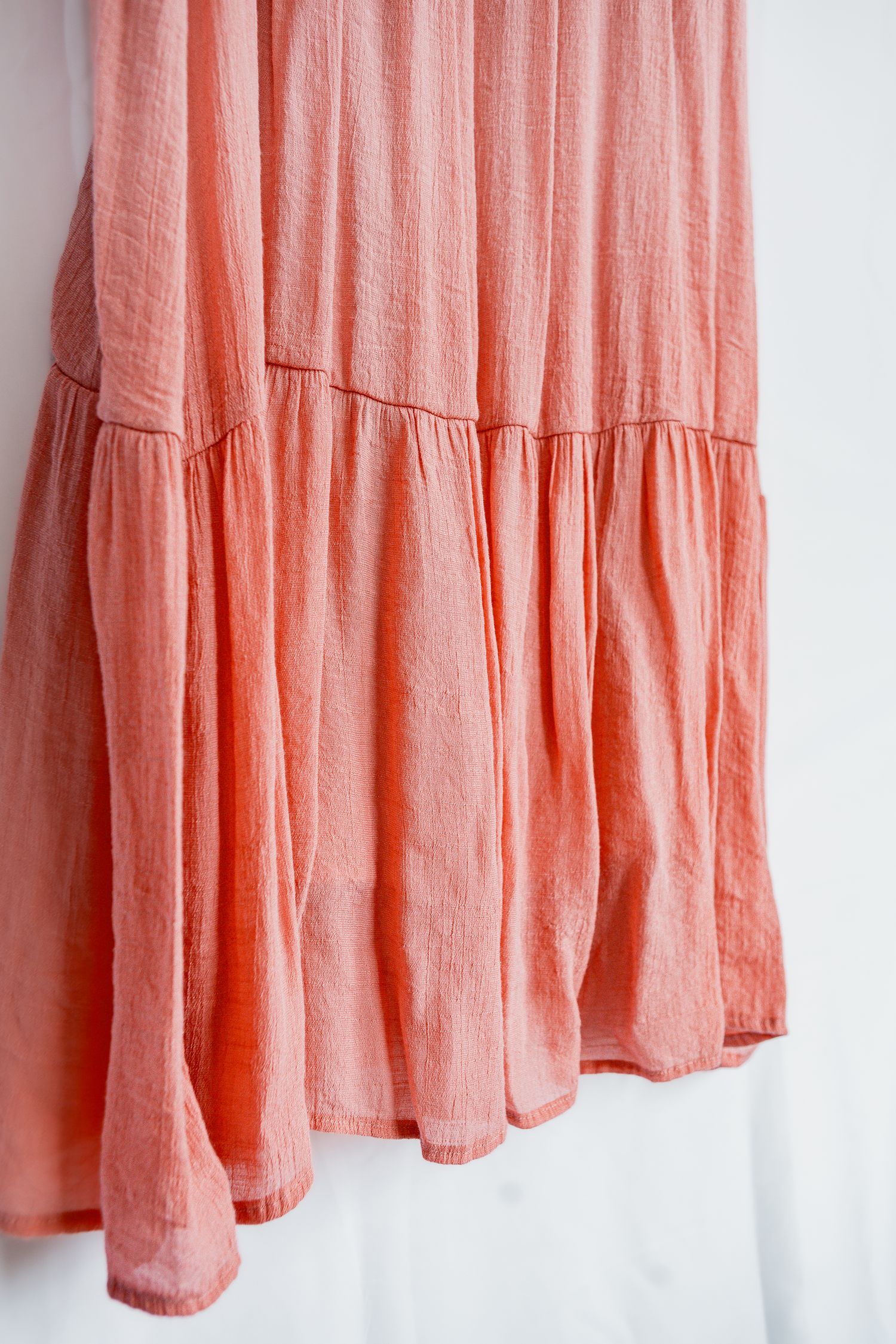 Soft peach linen dress with gathered ruffles and flowing skirt panels against white background.