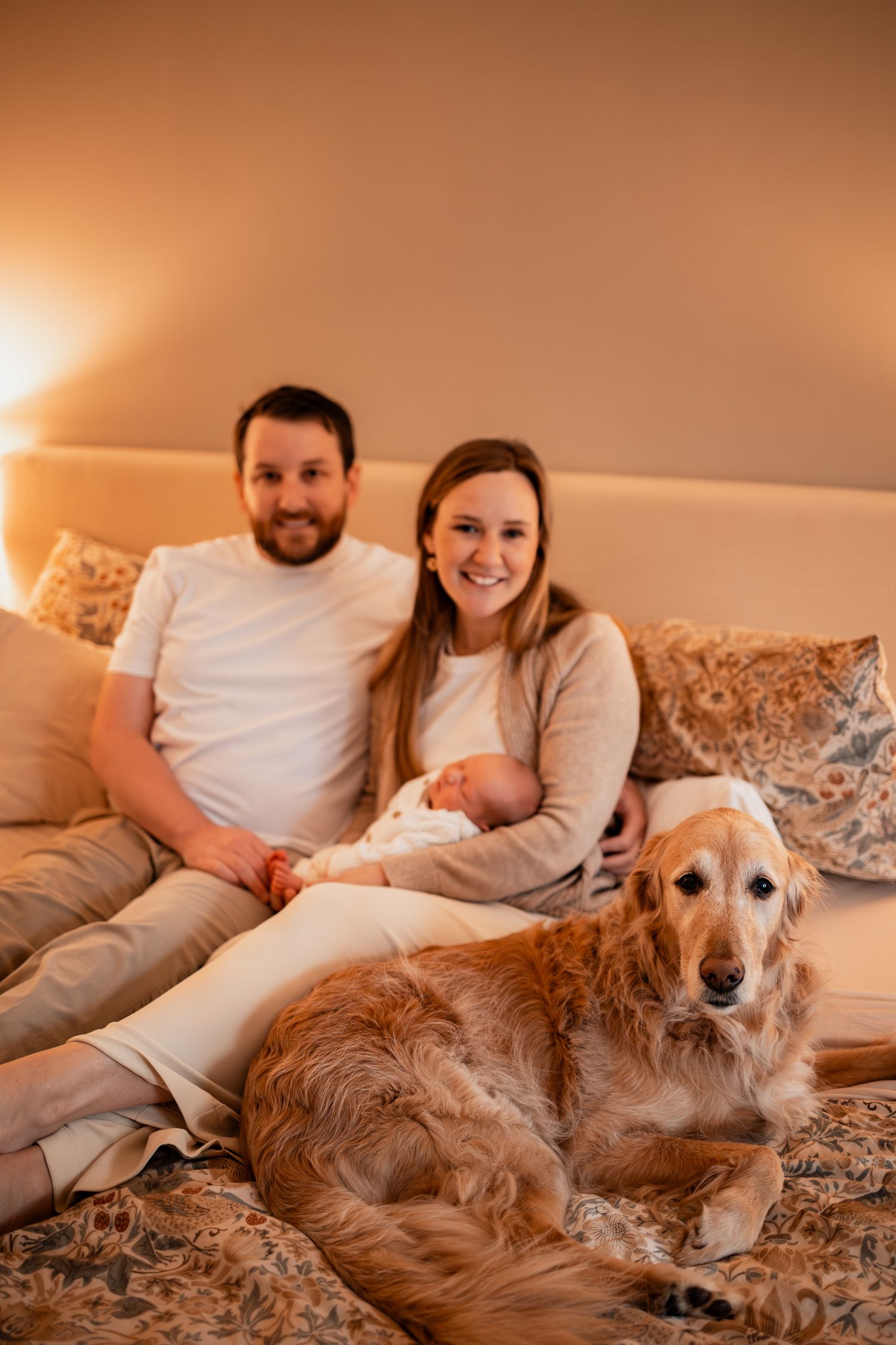 A golden retriever lies at the foot of a bed while its family relaxes together.