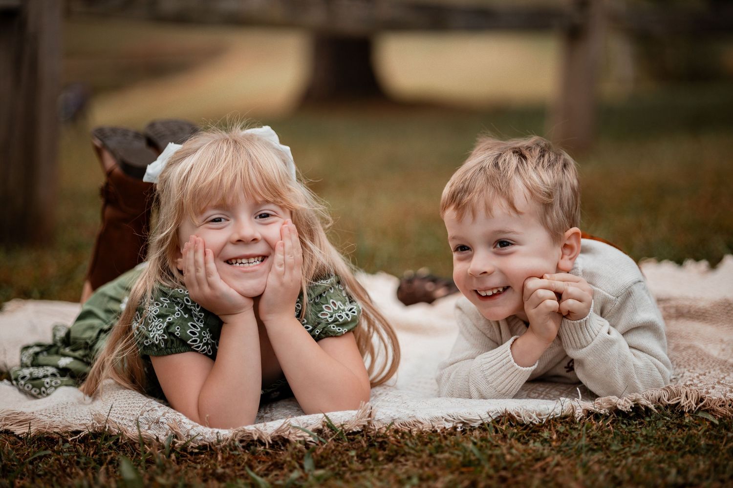 Children lie on the ground in a row with hands propped under chins during an outdoor photo session.