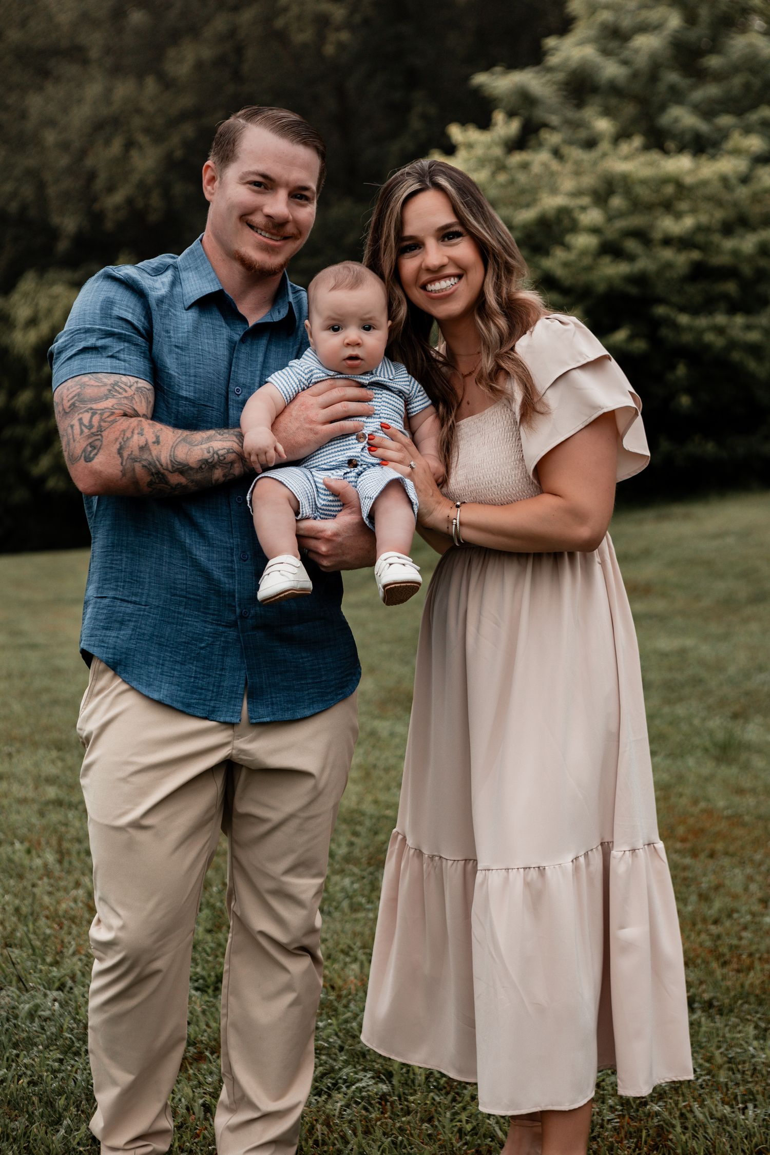 Casual outdoor family portrait session with parents and baby wearing matching neutral tones.