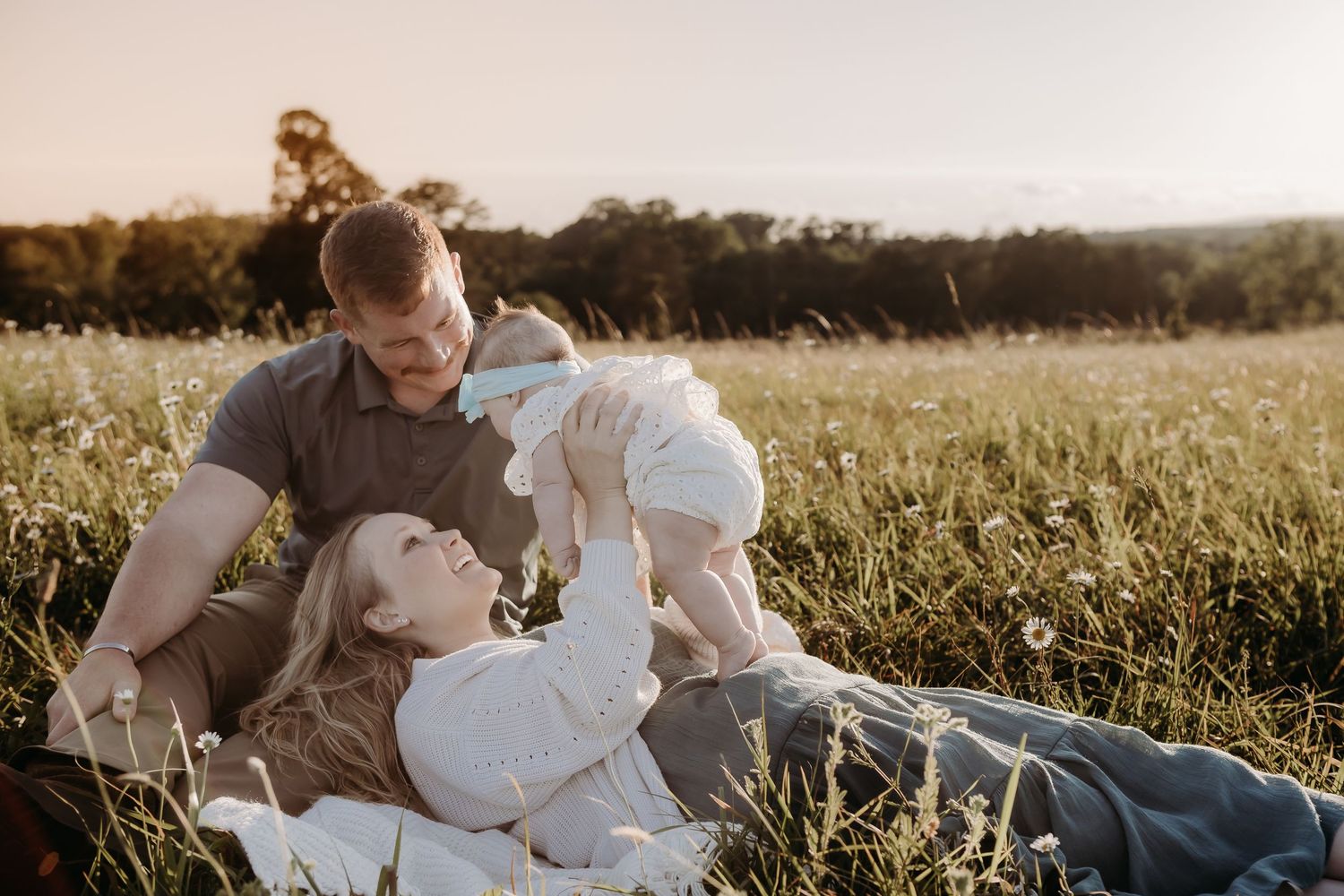 Family sharing intimate moments together while relaxing in a grassy field during golden hour.