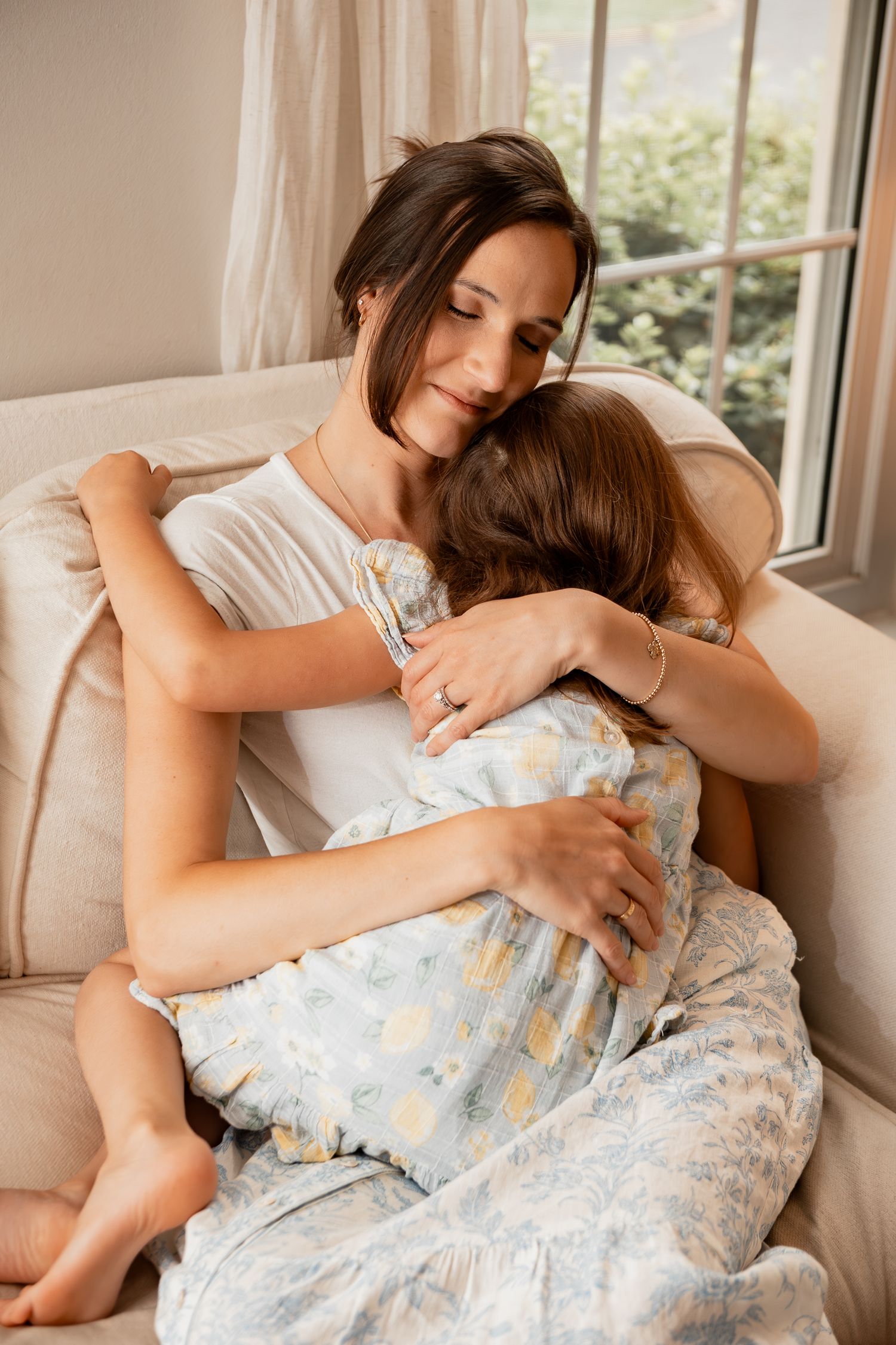 A tender embrace between a parent and child cuddling together on a cozy window-side couch.