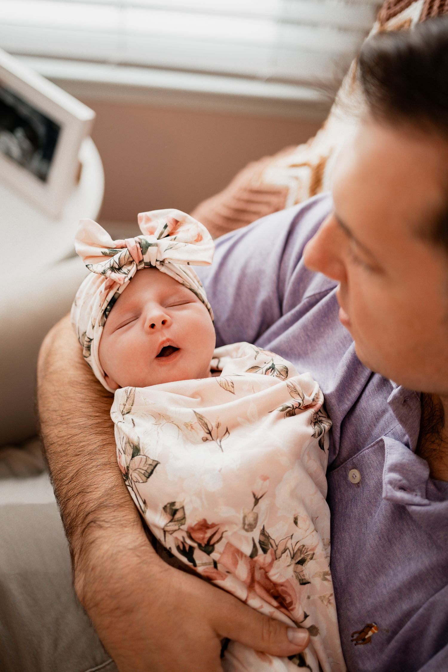 A newborn baby wearing a floral headband yawns while being held in a series of tender moments.