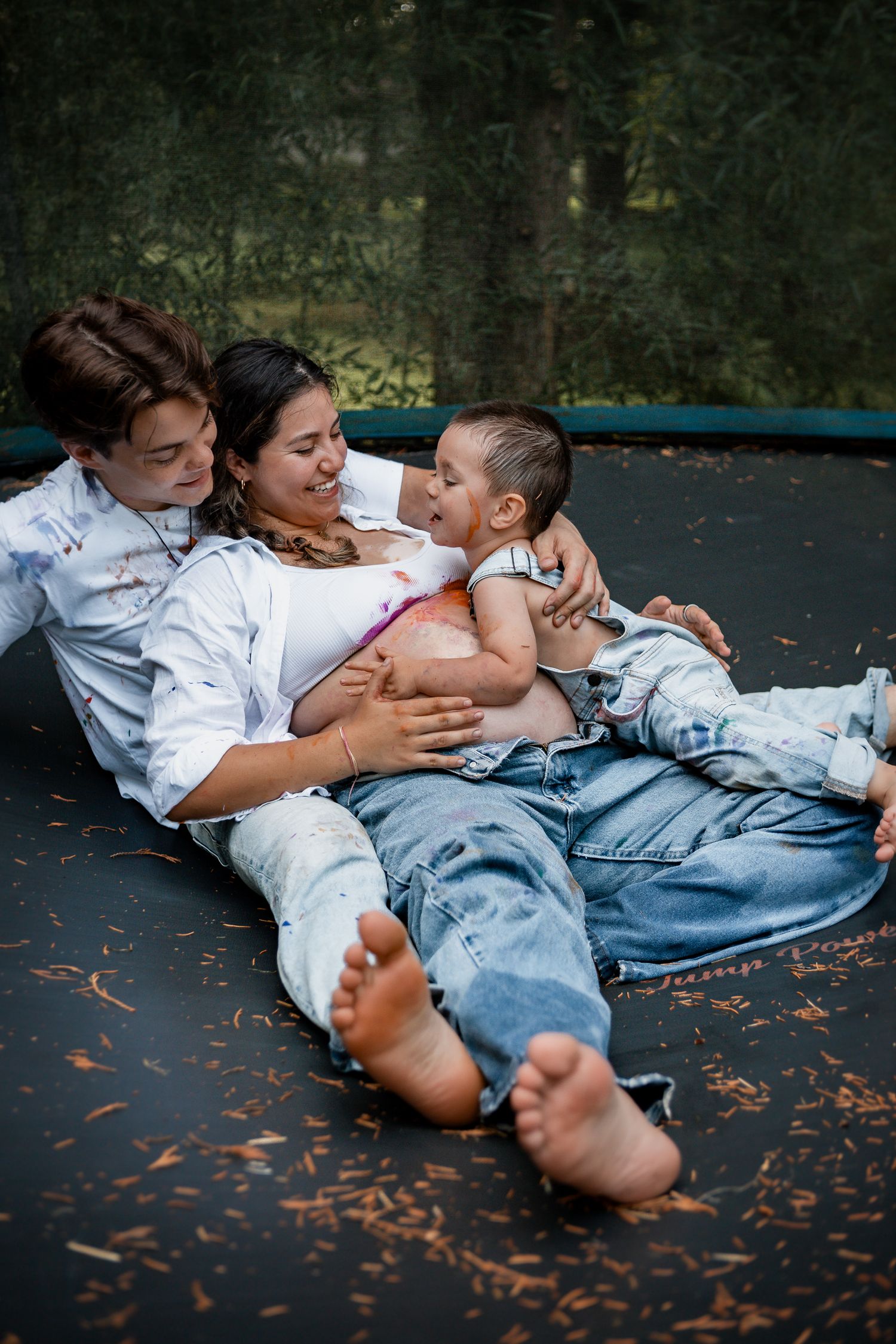 Family lying down on outdoor trampoline with scattered autumn leaves during intimate photoshoot.