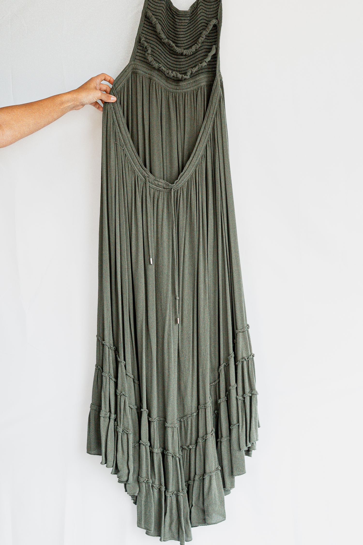Multiple views of an olive green boho dress with ruffle hem and delicate pleating details hanging against white background.